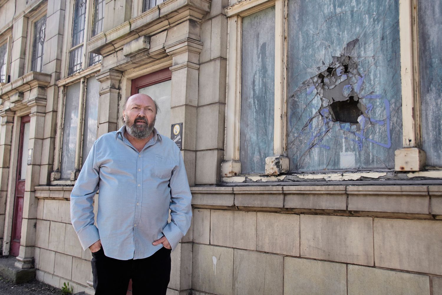 Person standing beside damaged building facade with broken windows.