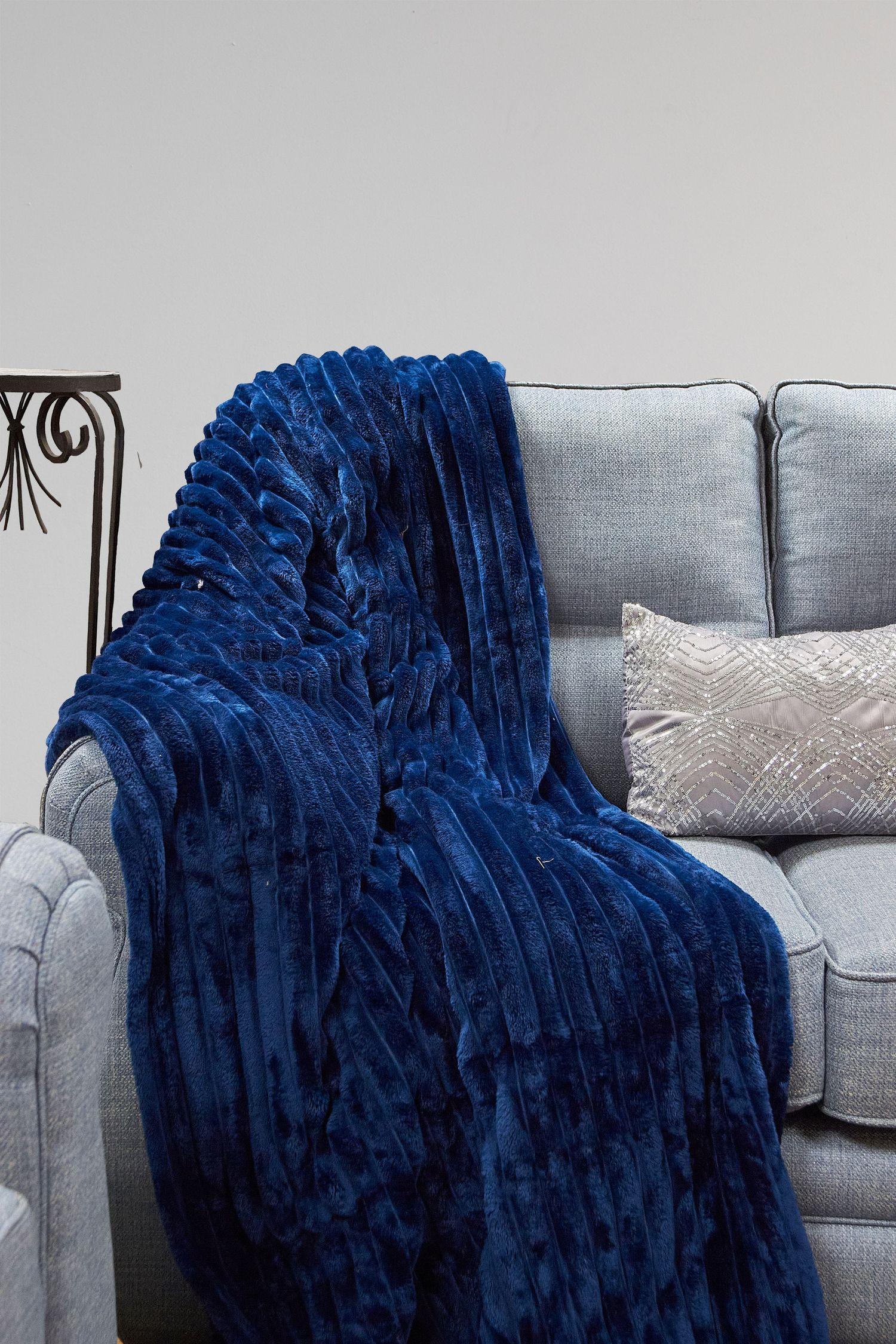 A plush navy blue faux fur throw blanket draped elegantly over a modern grey couch with decorative pillows.