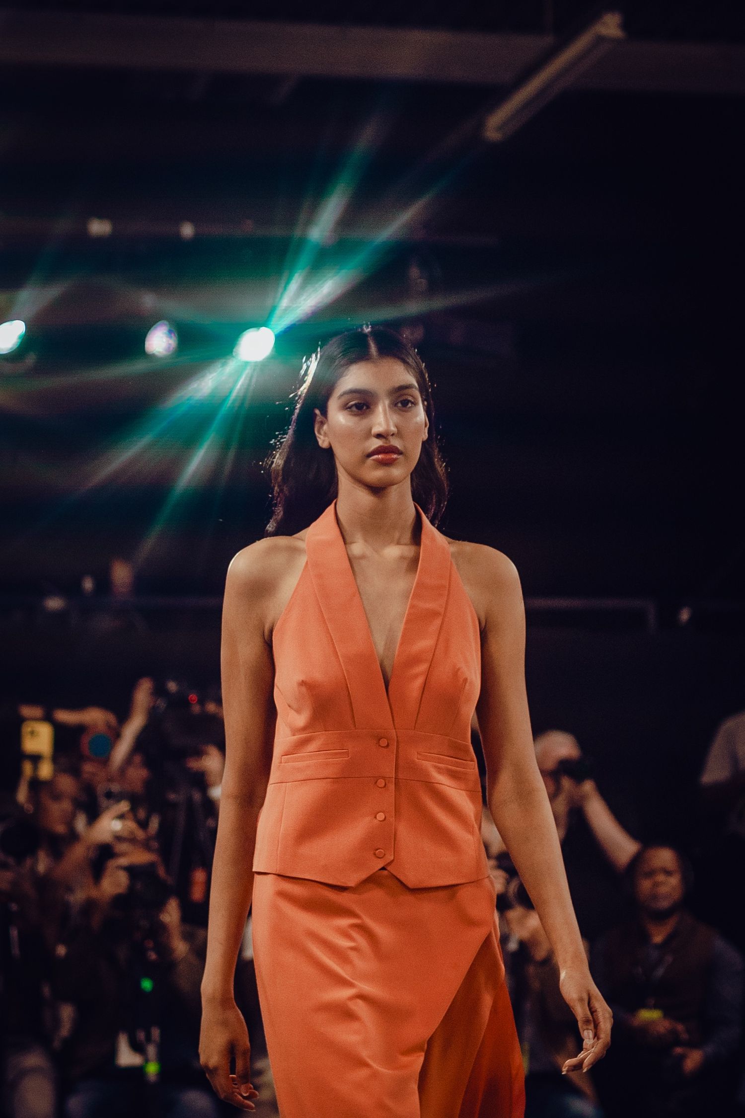 Sleek orange halter suit ensemble displayed on fashion runway with dramatic lighting.