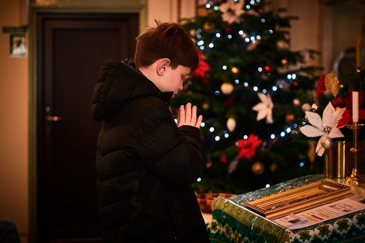 Person praying near a decorated Christmas tree with wrapped presents.