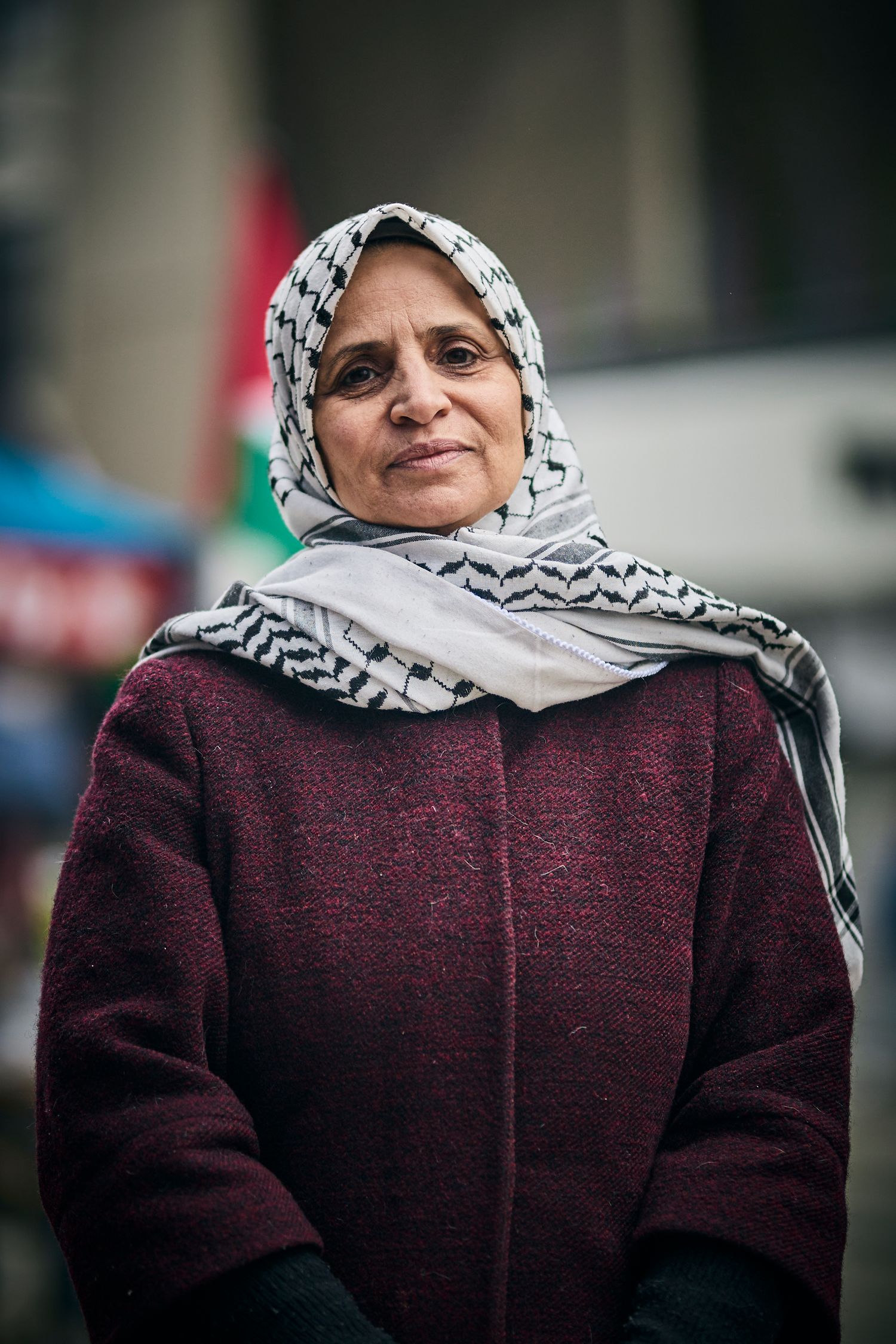 Woman wearing traditional headscarf and burgundy coat at outdoor protest event.