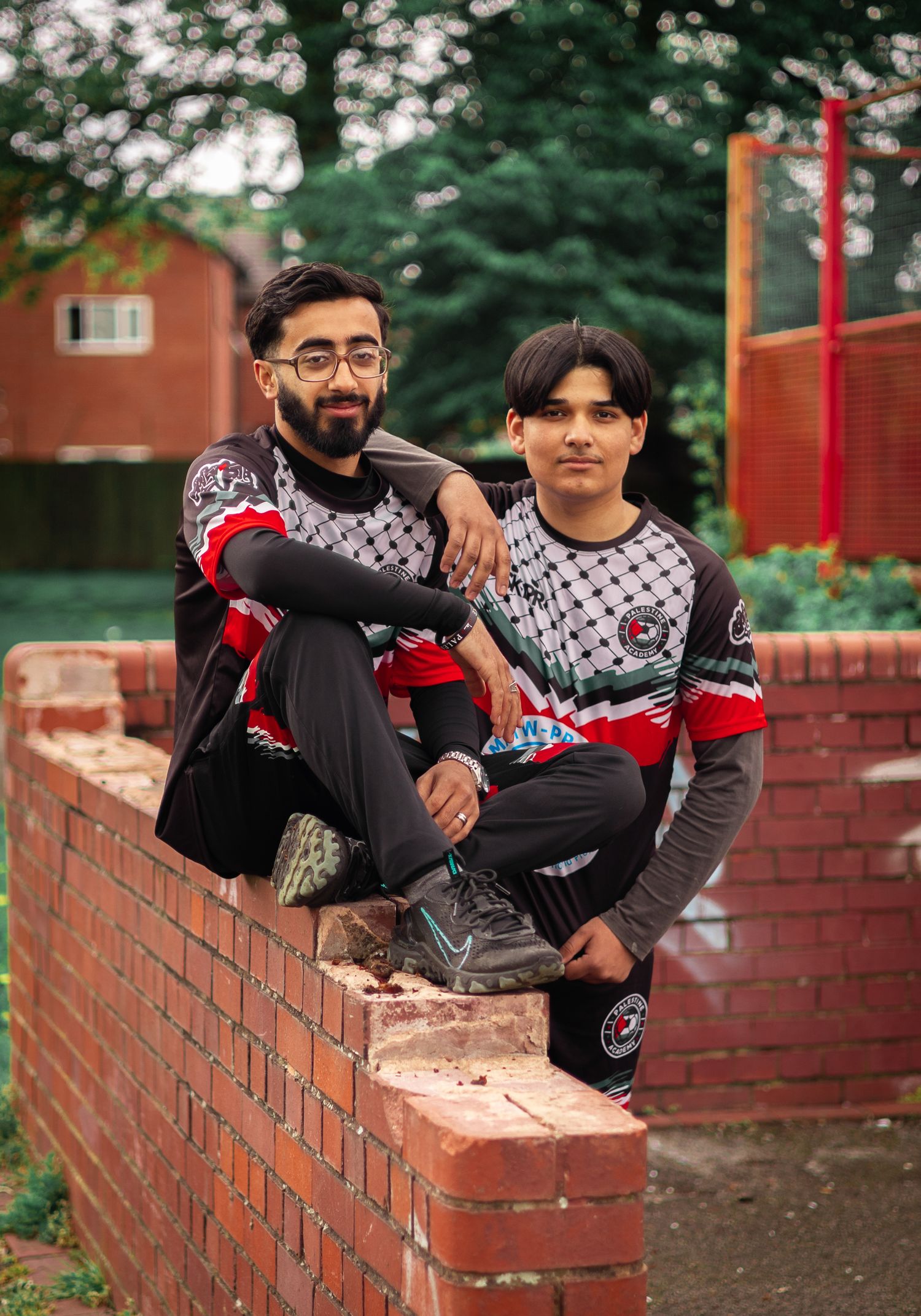 Soccer teammates in coordinated uniforms sitting casually on red brick wall.