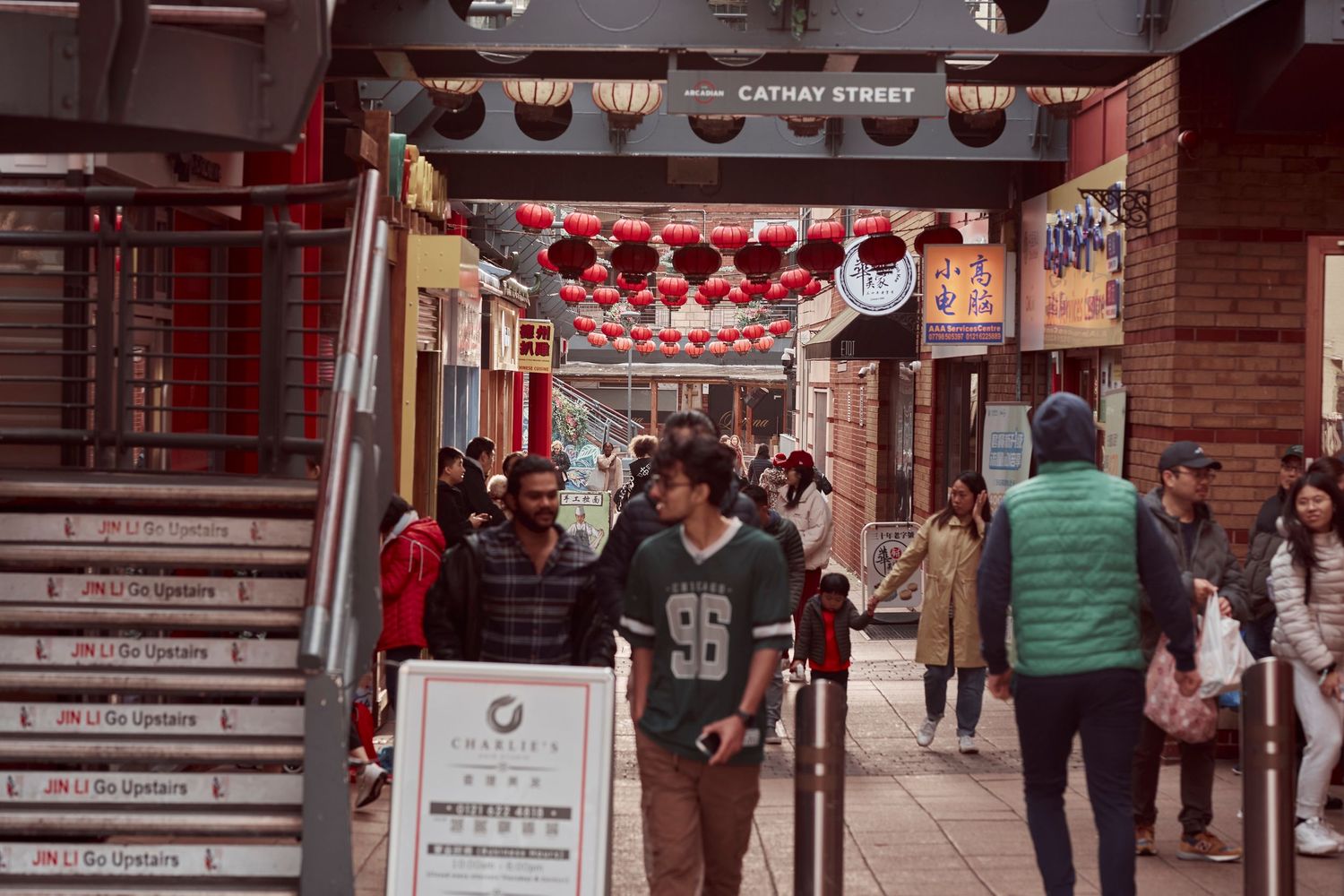 A busy street market with red lanterns hanging overhead and shoppers walking through.