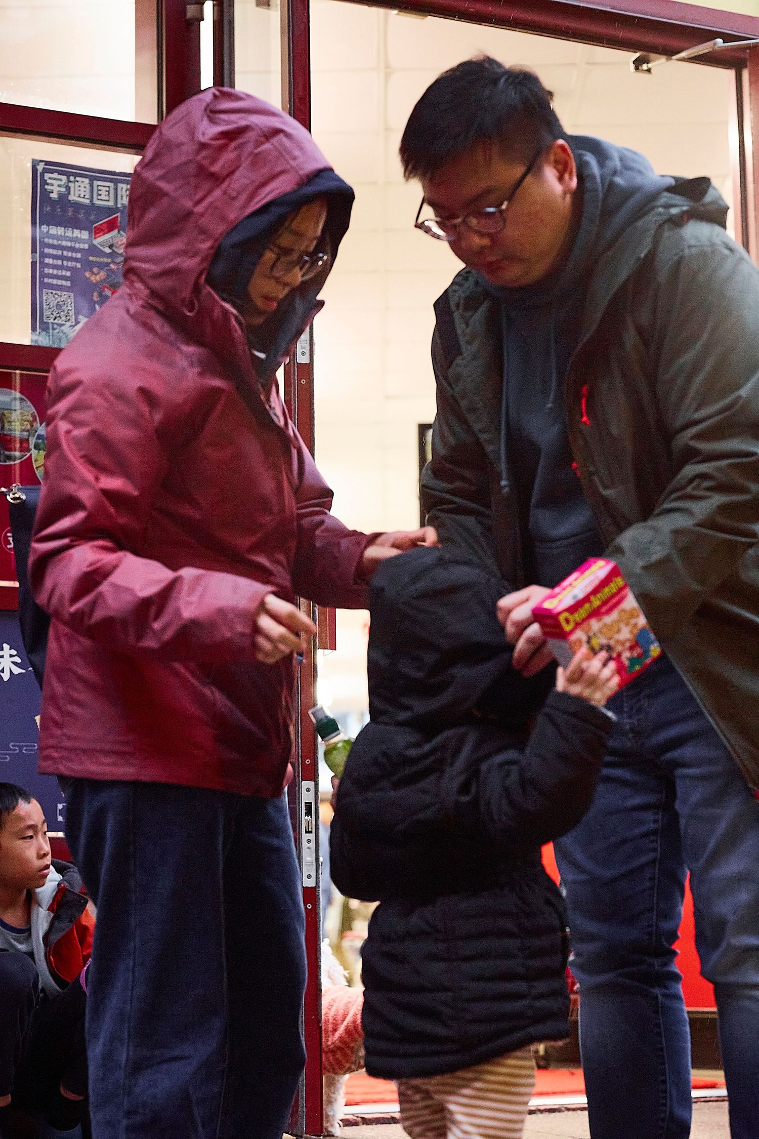 People in winter coats examining items under red lanterns during rainy weather.