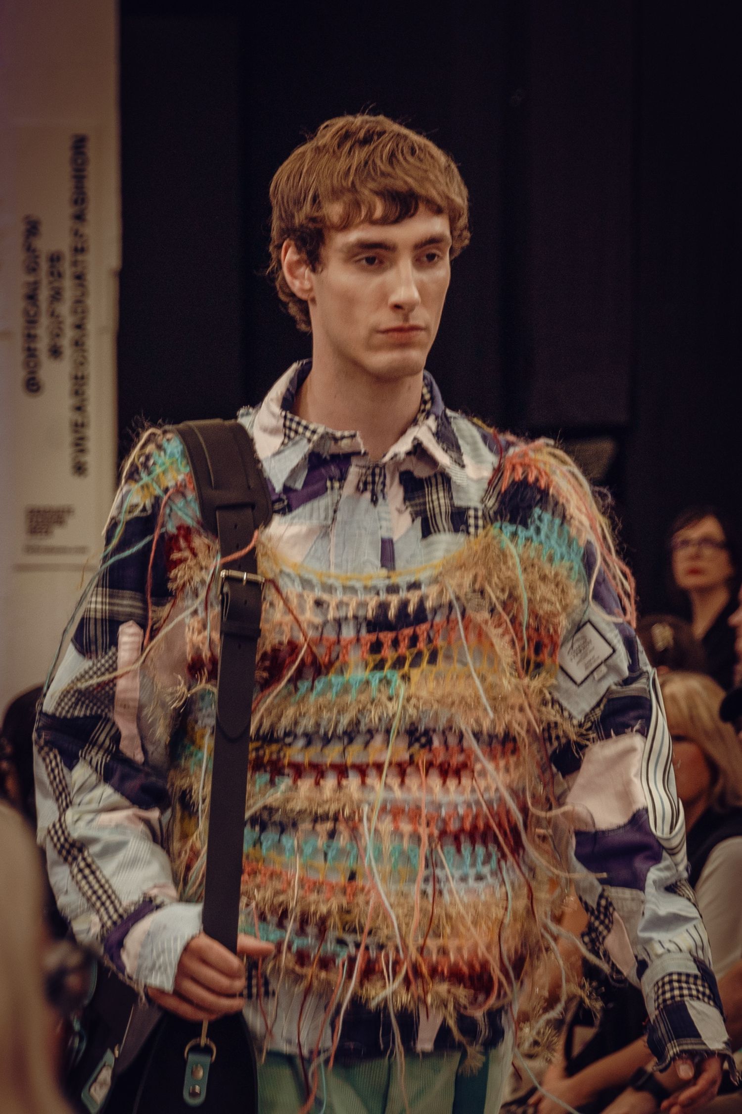 Model wearing patterned multicolor sweater with backpack on fashion runway.