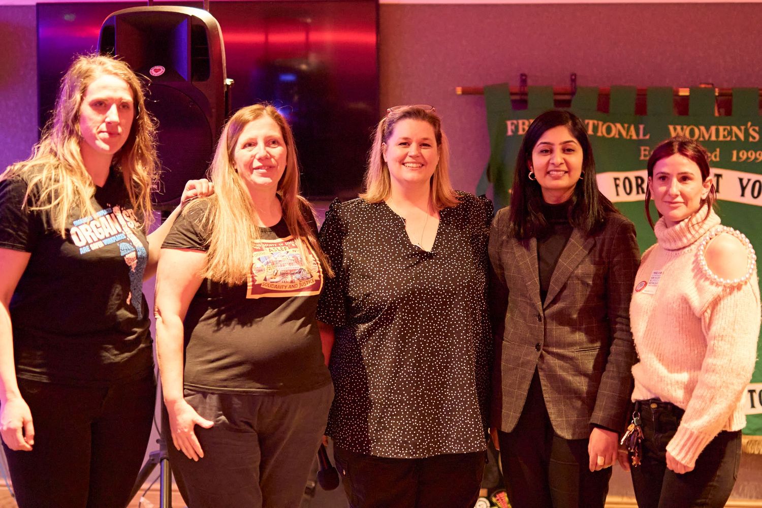 A group of five people pose together at an event with red and pink lighting in the background.