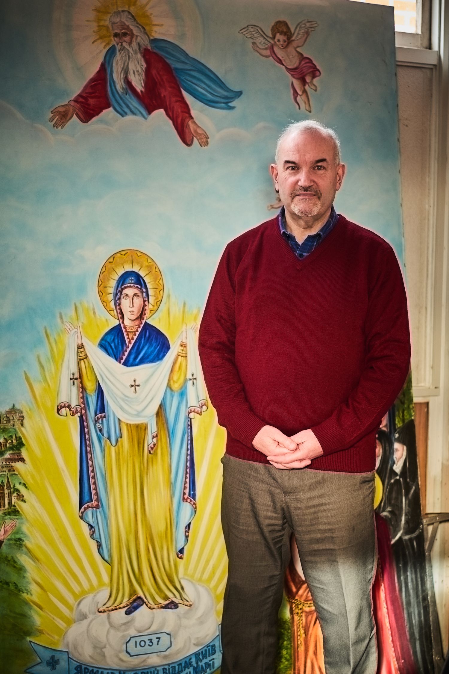 Religious mural with angels and saints serving as backdrop for portrait in red sweater.