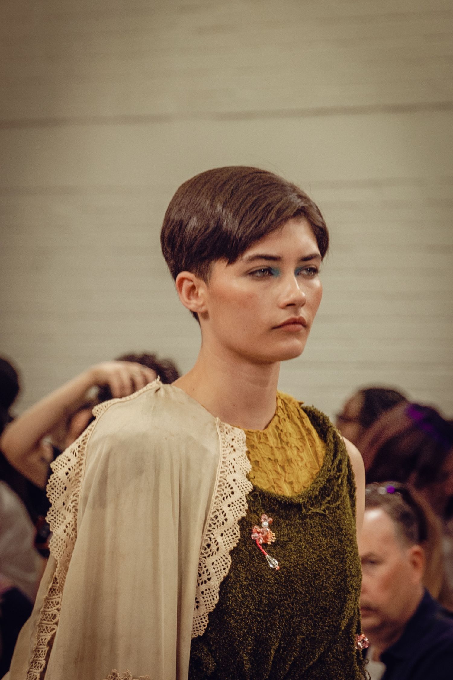 Model wearing vintage-inspired dress with lace details and mustard accent on runway.