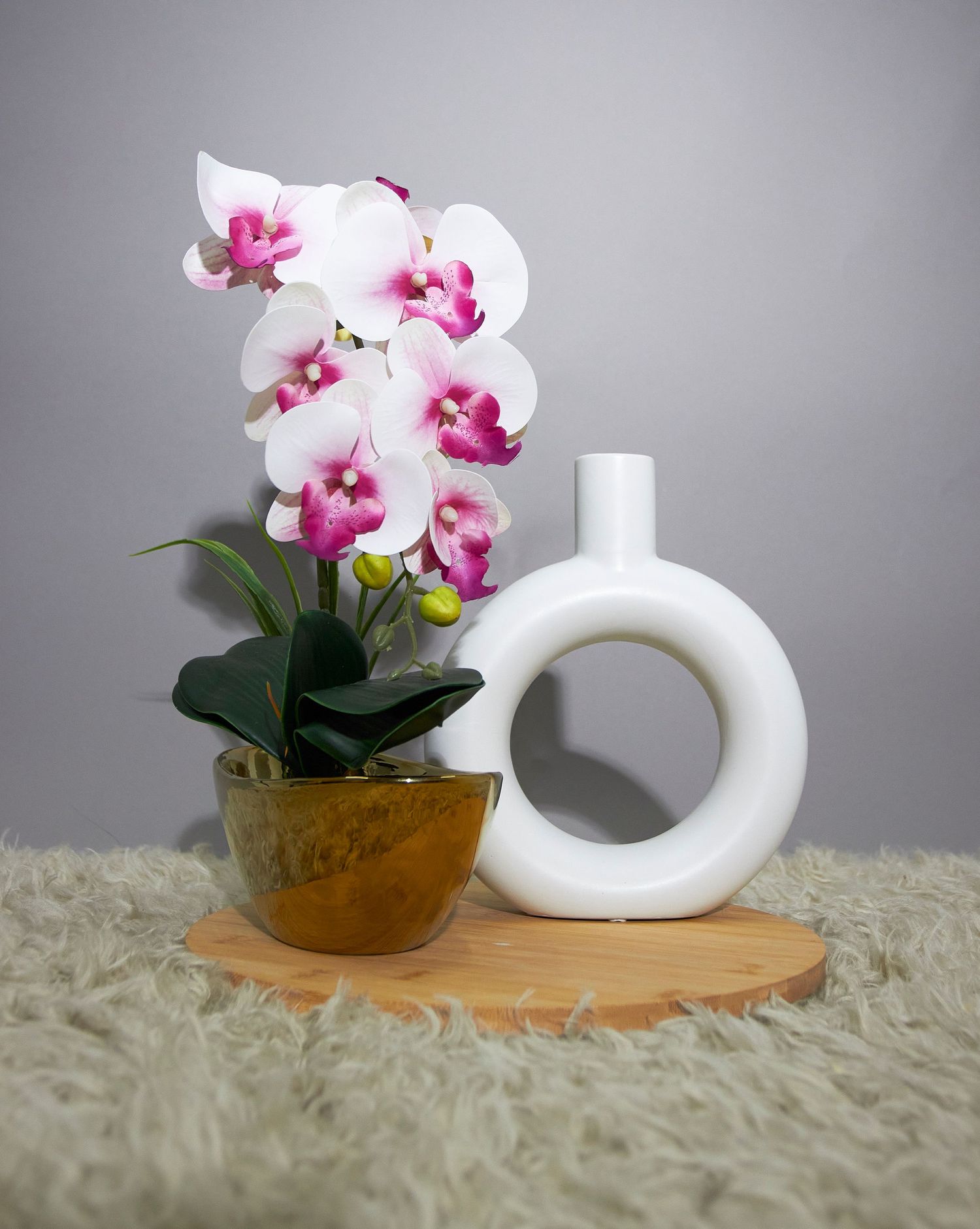Abstract wave-like white sculpture with pink and white orchid plant in brown pot on light carpet.