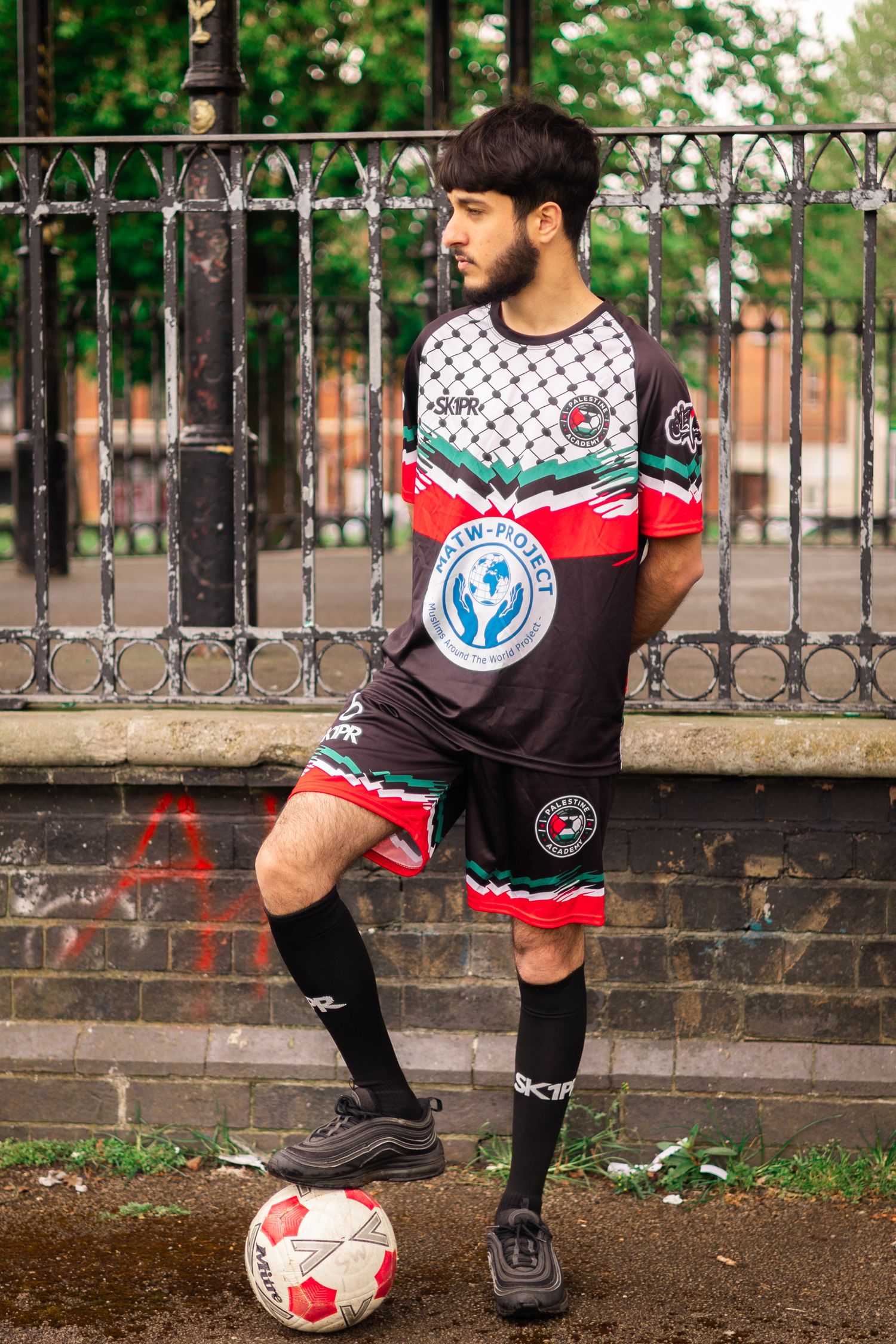 Player in geometric patterned jersey poses with ball by iron fence.