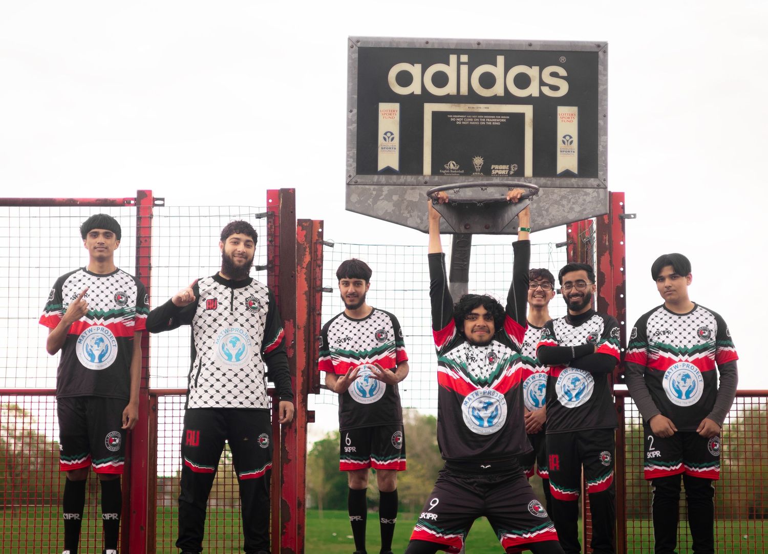 Soccer team poses together under Adidas basketball backboard wearing matching uniforms.