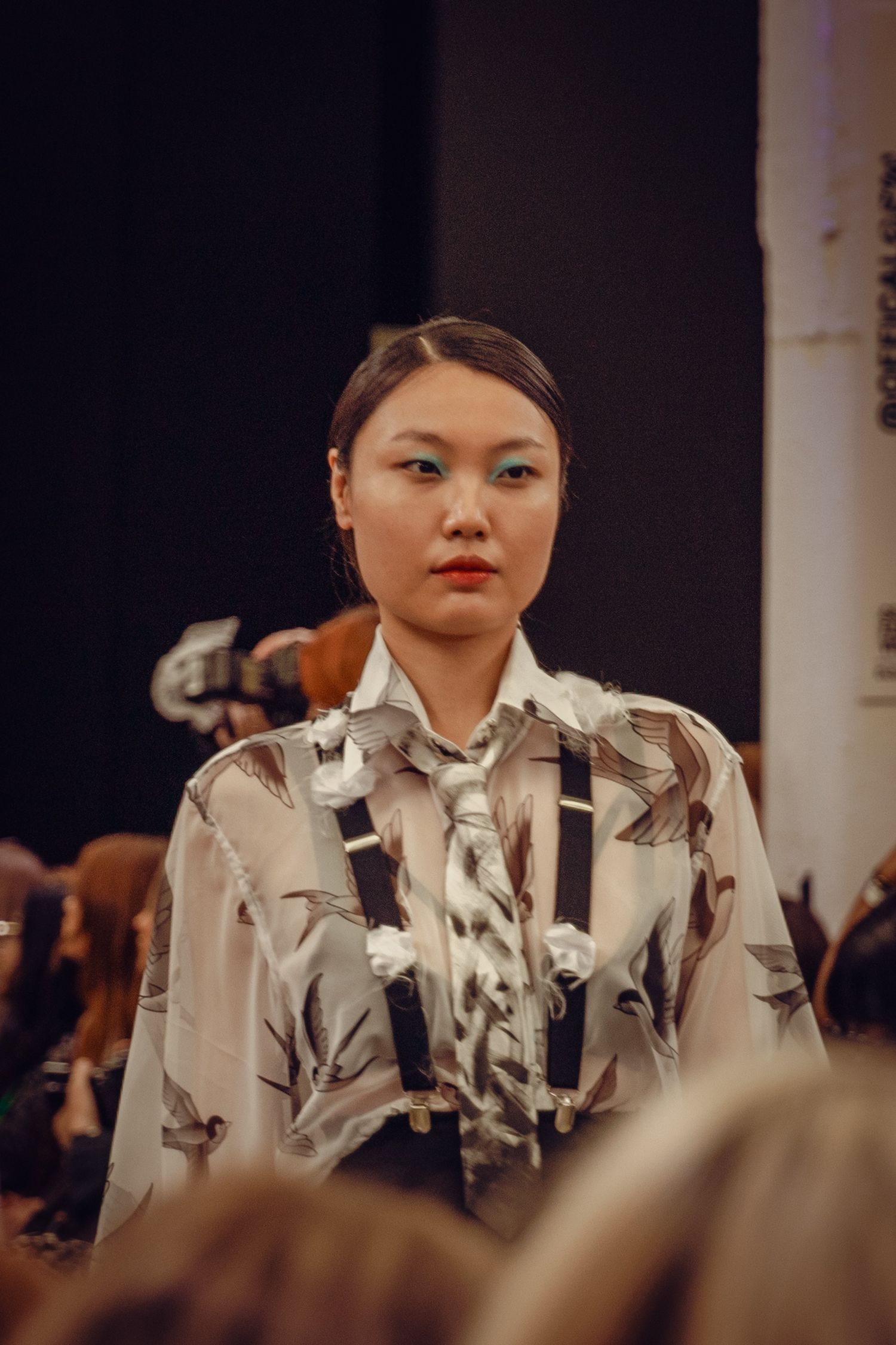 Model presents floral printed blouse with black straps on fashion runway.