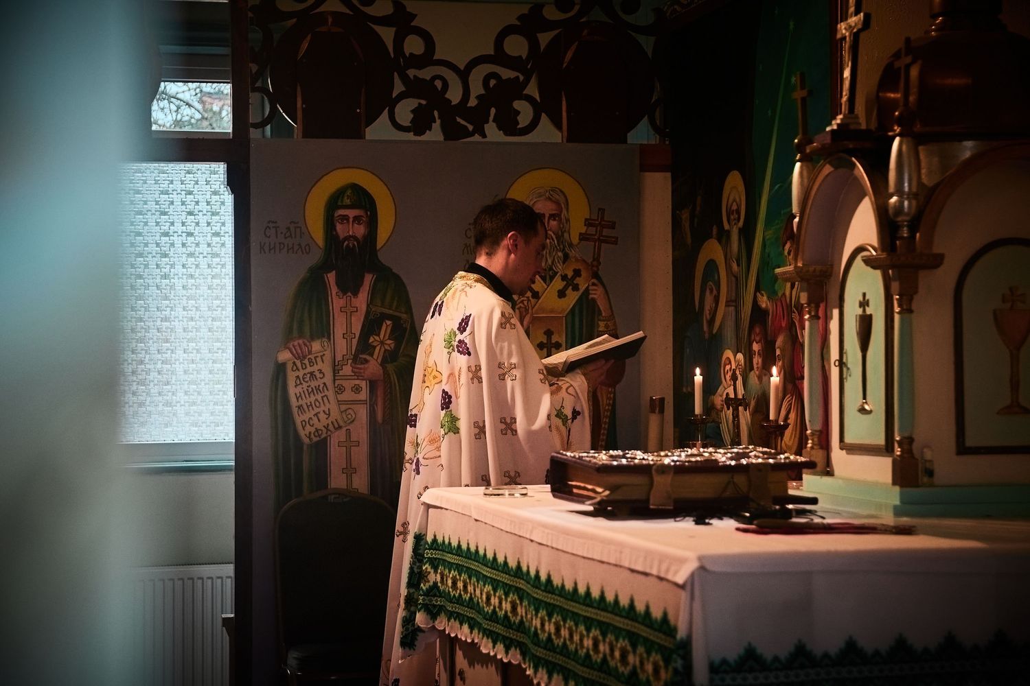 Priest reading from sacred texts at an ornate altar with religious icons in the background.