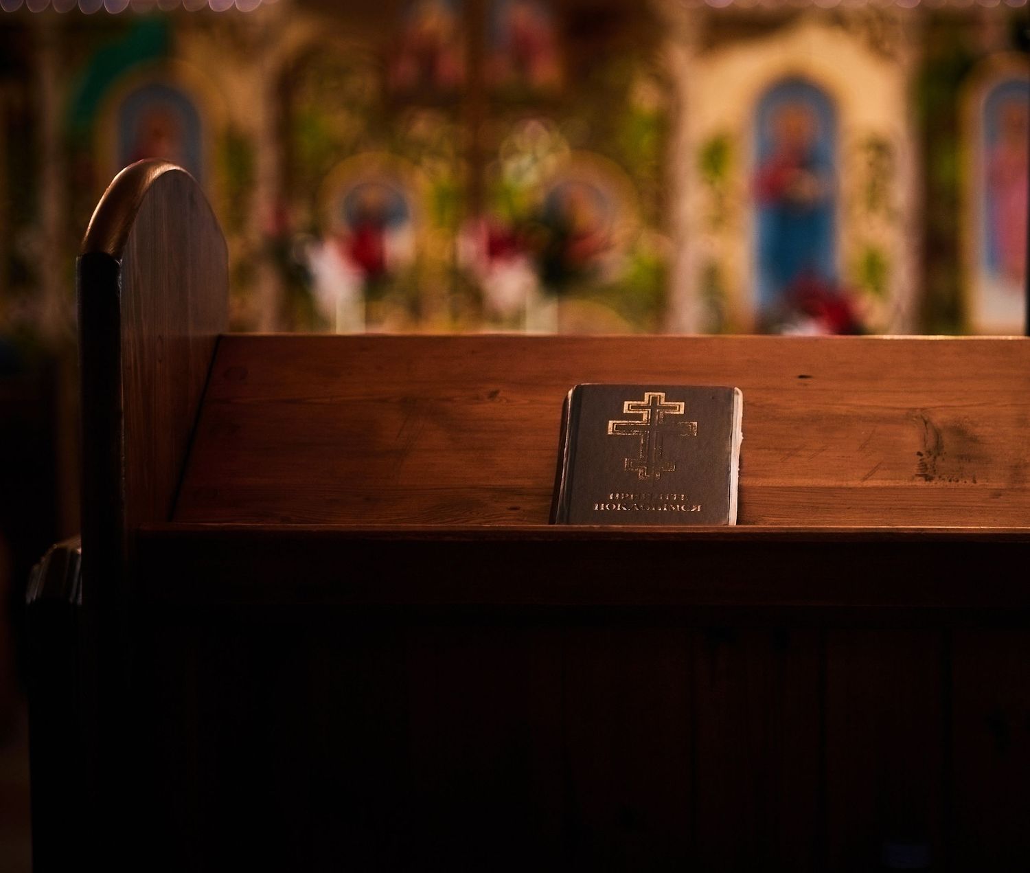 A holy Bible resting on a wooden church pew with colorful stained glass windows in the background.