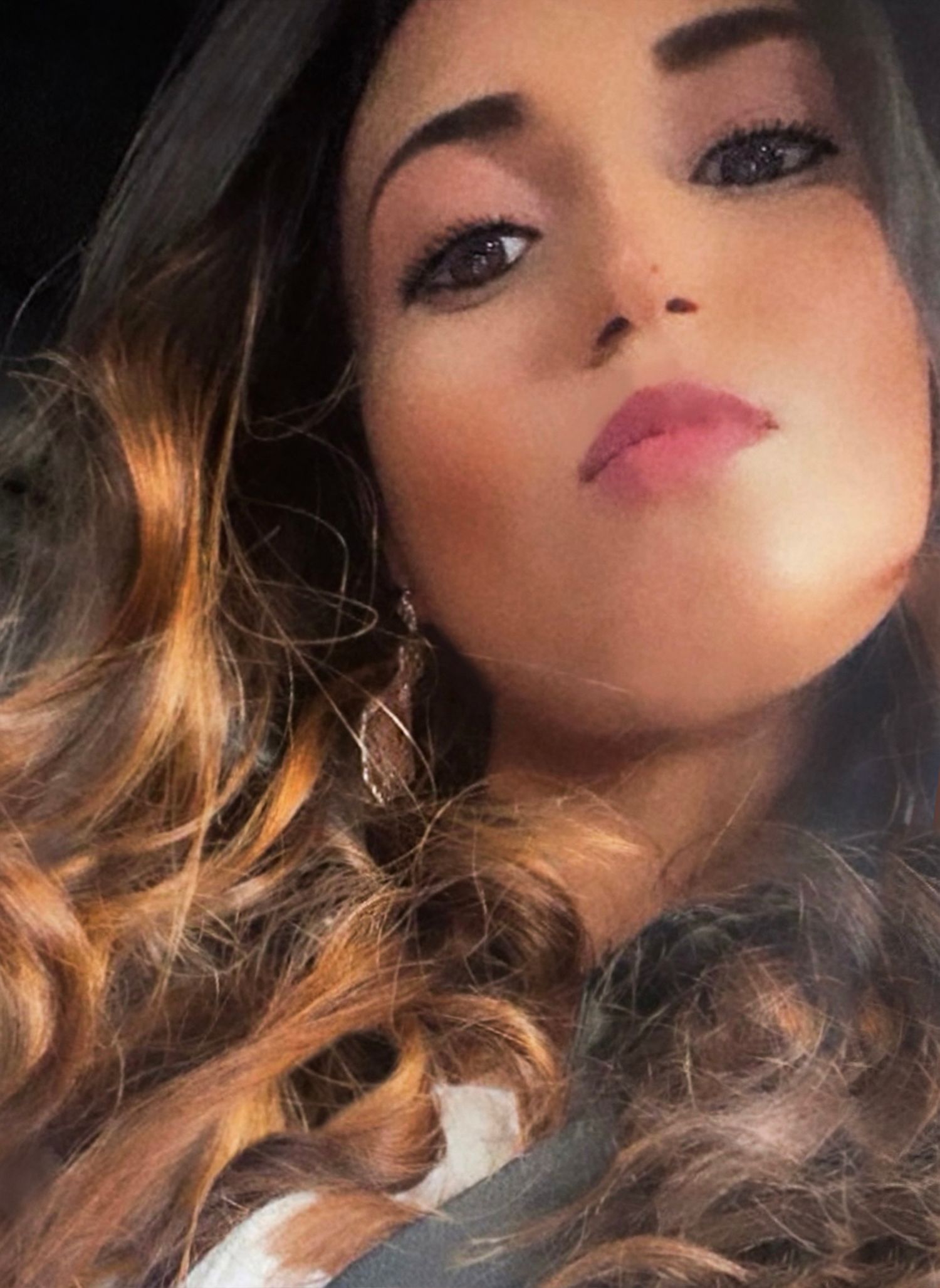 Close-up beauty shot with soft lighting showing wavy brown hair, pink lipstick and dramatic eye makeup.