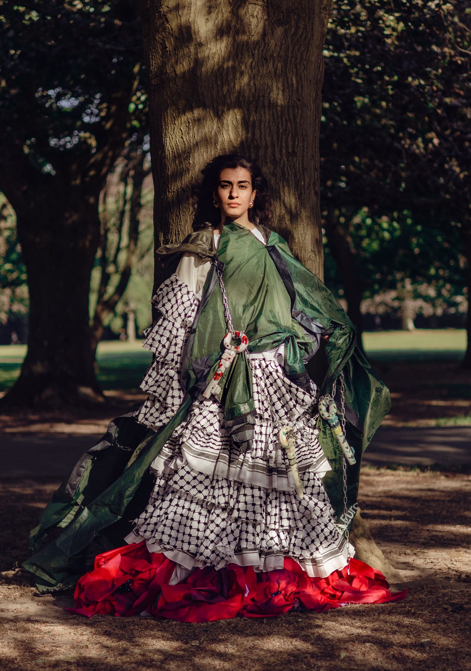 A dramatic layered dress with green silk overlay, black and white checkered ruffles, and red tulle bottom in a forest setting.