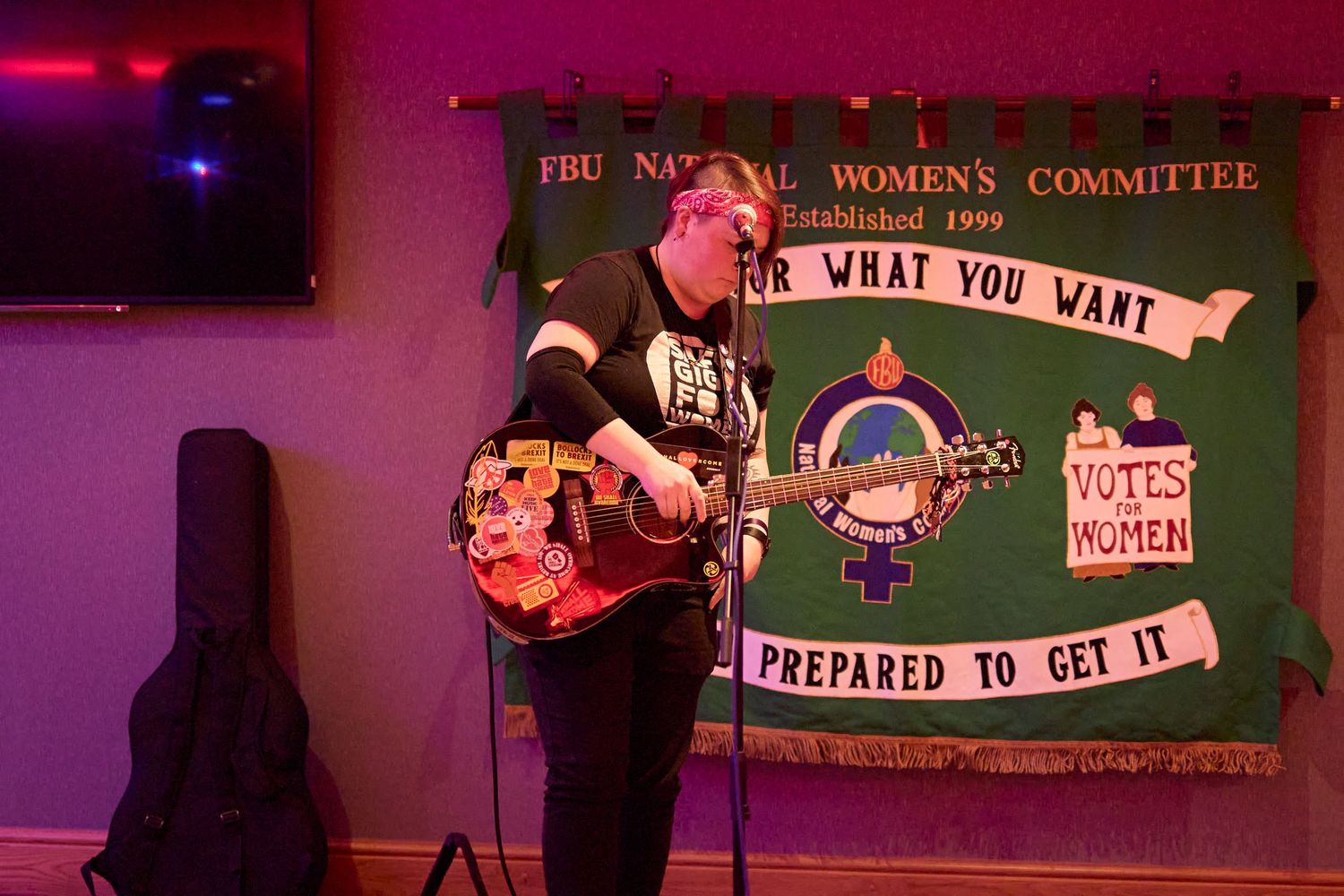 A dimly lit bar or venue space bathed in red lighting with colorful banners and signs hanging on the walls.