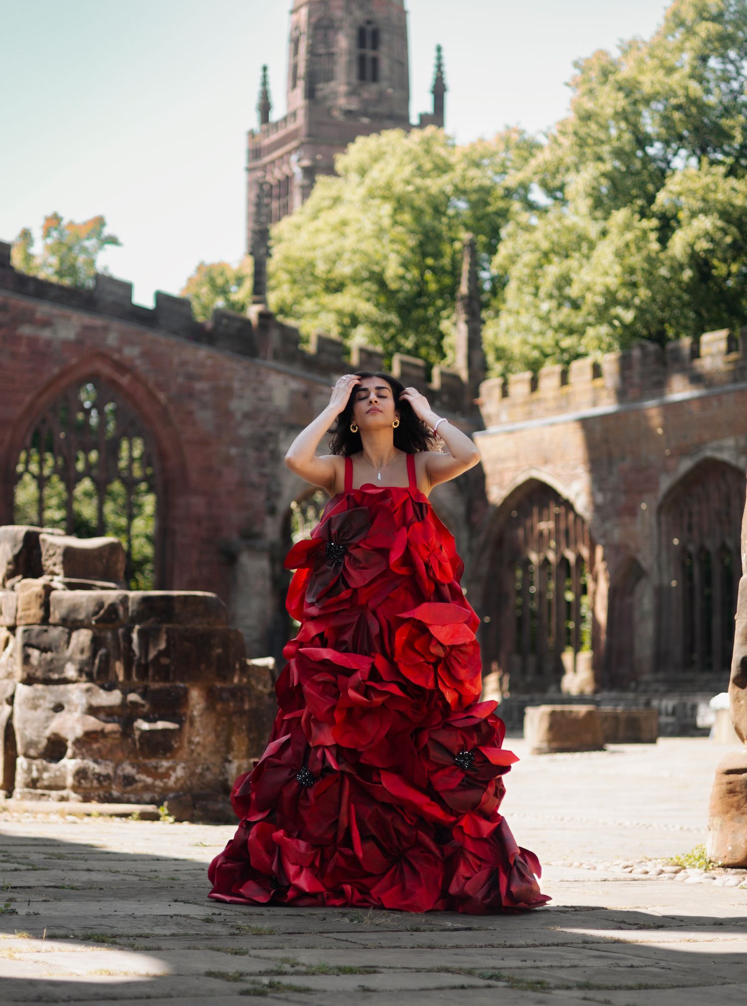A dramatic red ruffled ball gown photographed against gothic church architecture on a sunny day.