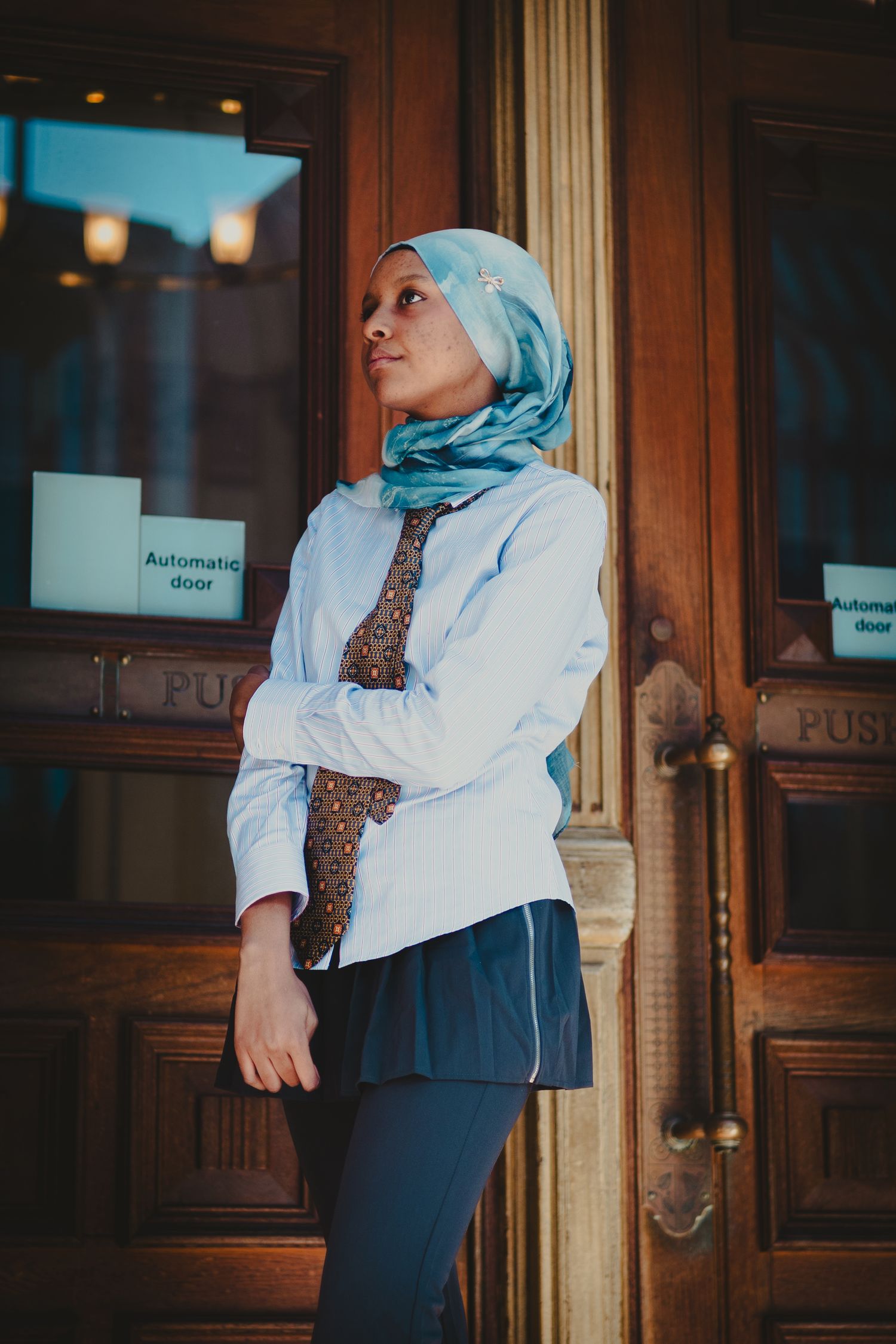 Fashion portrait showing business attire with turquoise hijab against ornate wooden background.