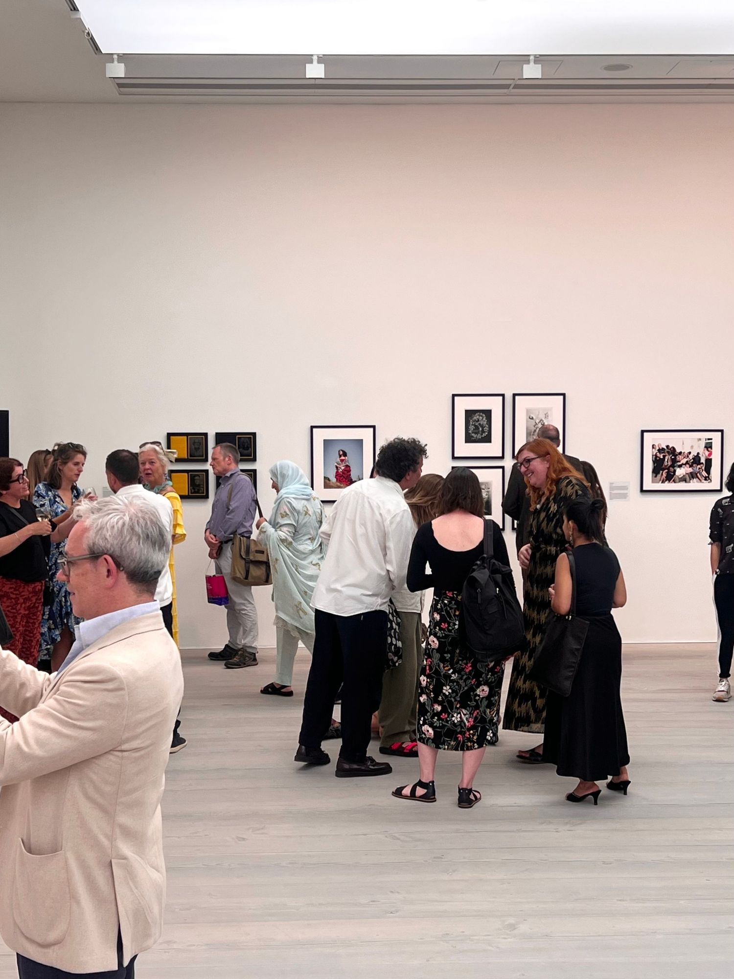 Guests mingle at an art gallery opening, viewing framed photographs on white walls in a modern exhibition space.