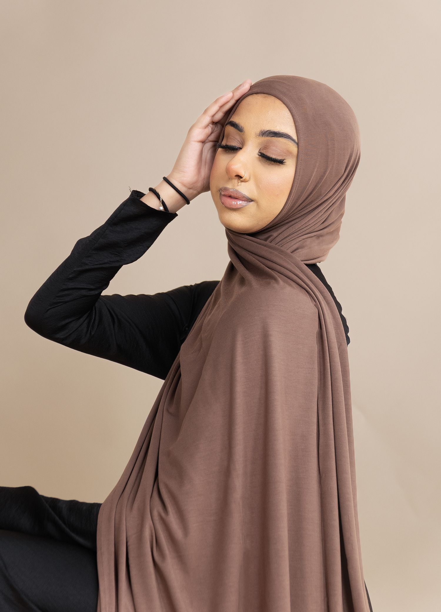 Model wearing brown hijab and black long sleeve top poses in series of graceful side profile shots against neutral background.