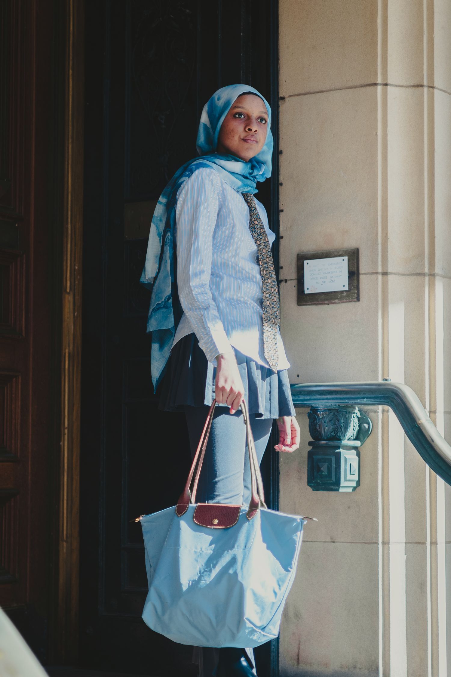 Casual business attire with light blue headscarf, white shirt and tote bag near stone column.