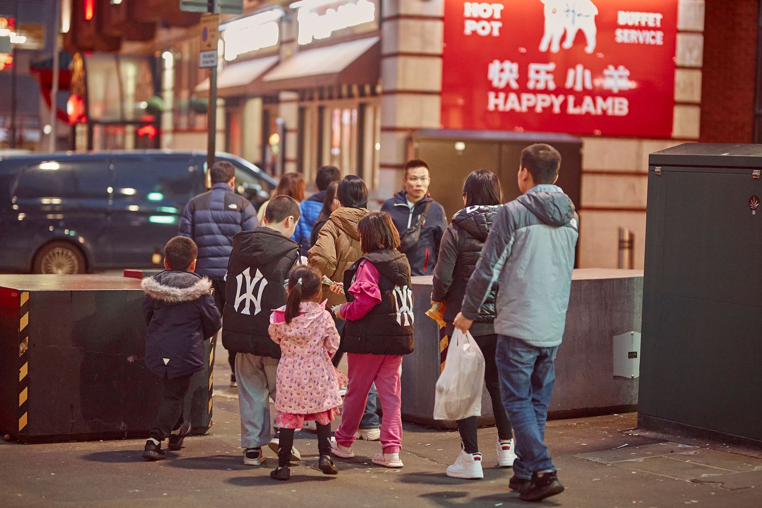 People walking past storefront signs in Chinatown with neon lights and red decor.