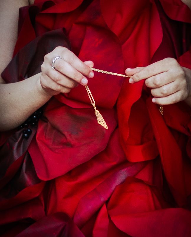 Hands holding a delicate gold necklace against a backdrop of vibrant red rose petals.