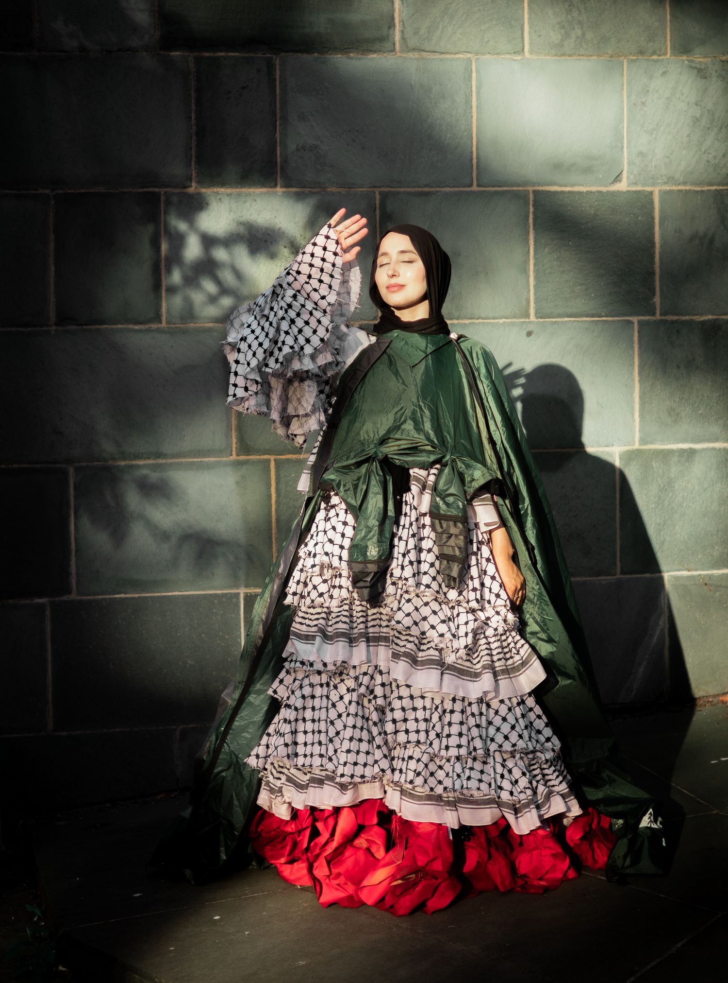 A dramatic fashion series showing a model in a ruffled dress with green cape against a dark stone wall background.