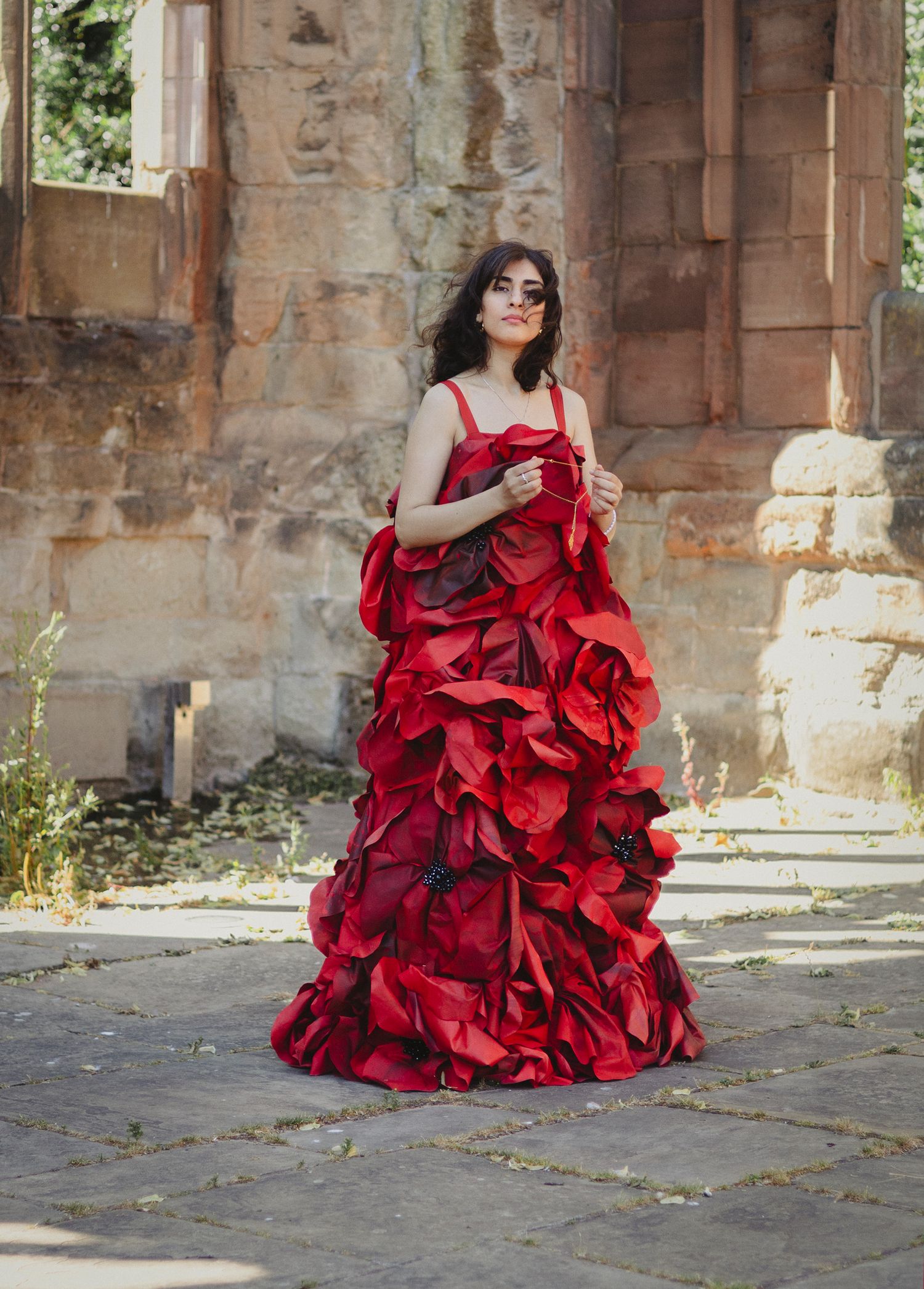 Dramatic red ruffled gown photographed against weathered stone architecture and greenery.