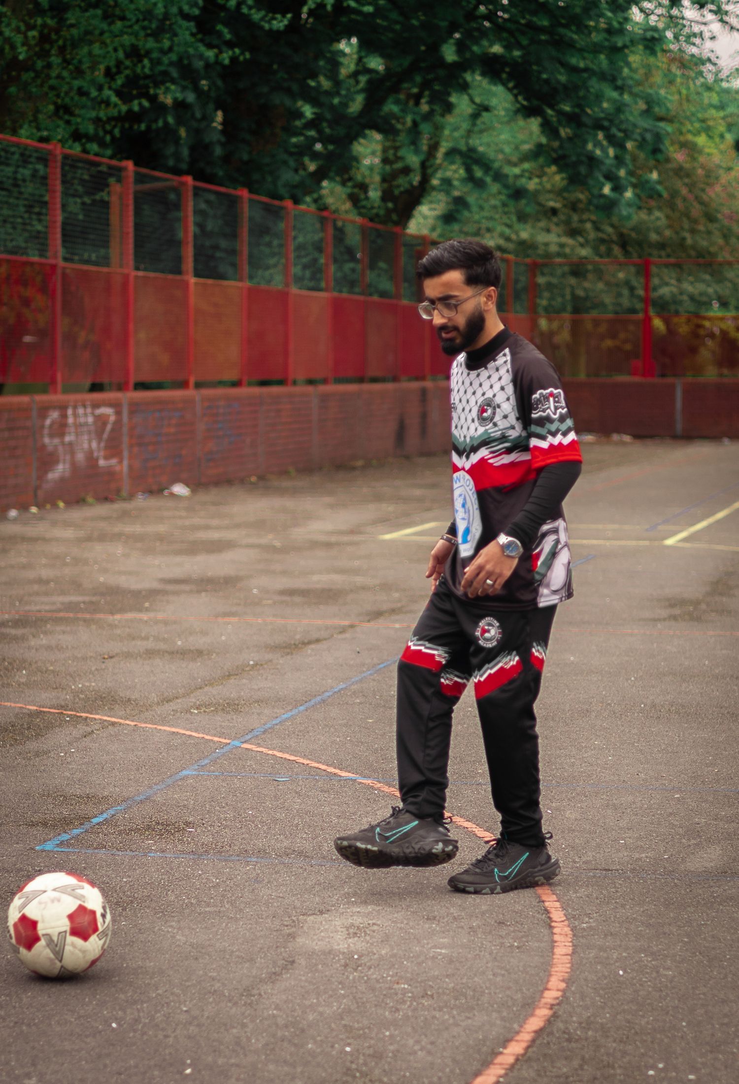 An athlete in a black and white patterned uniform prepares to kick a soccer ball on an outdoor court.