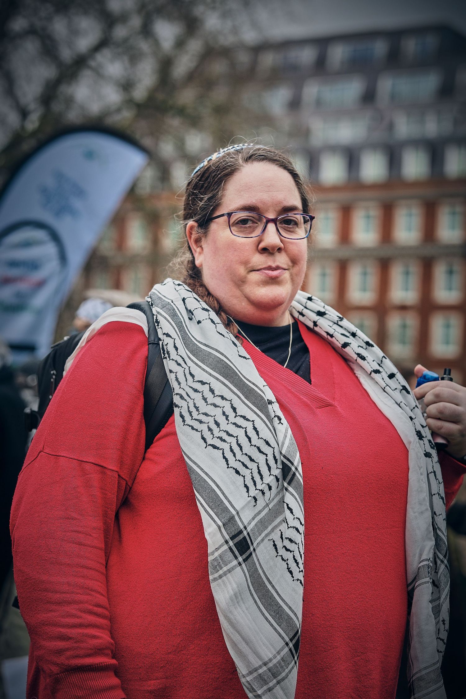 Person in red sweater and traditional keffiyeh scarf at outdoor gathering.