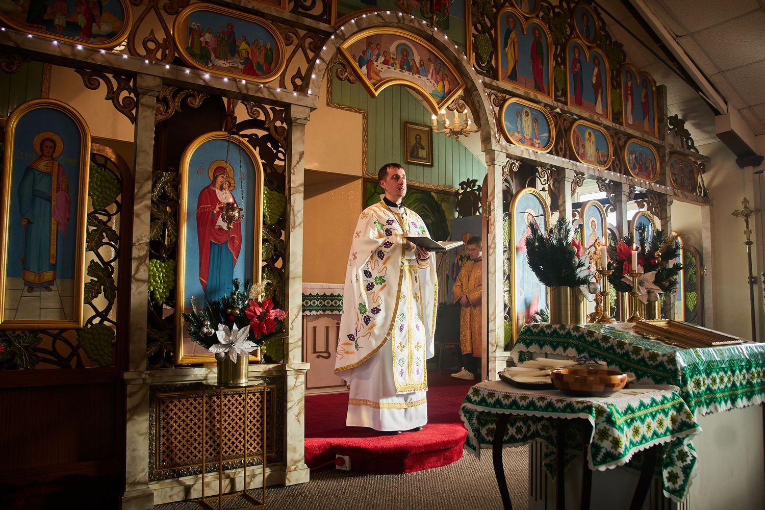 Orthodox church interior with religious icons and Christmas greenery illuminated by candlelight.