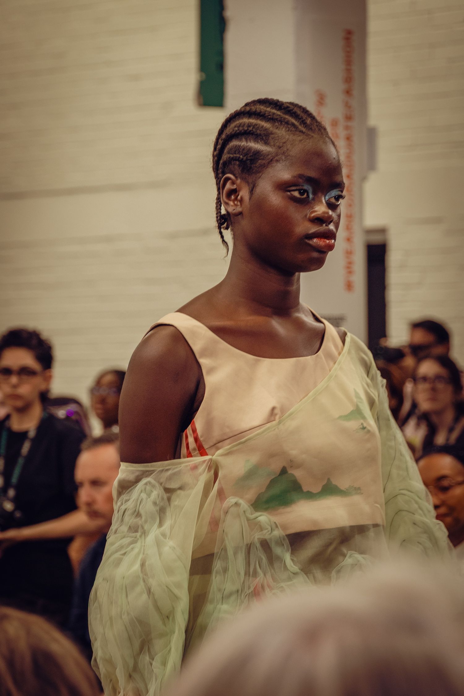 Model wearing ethereal cream colored draped dress on fashion runway.