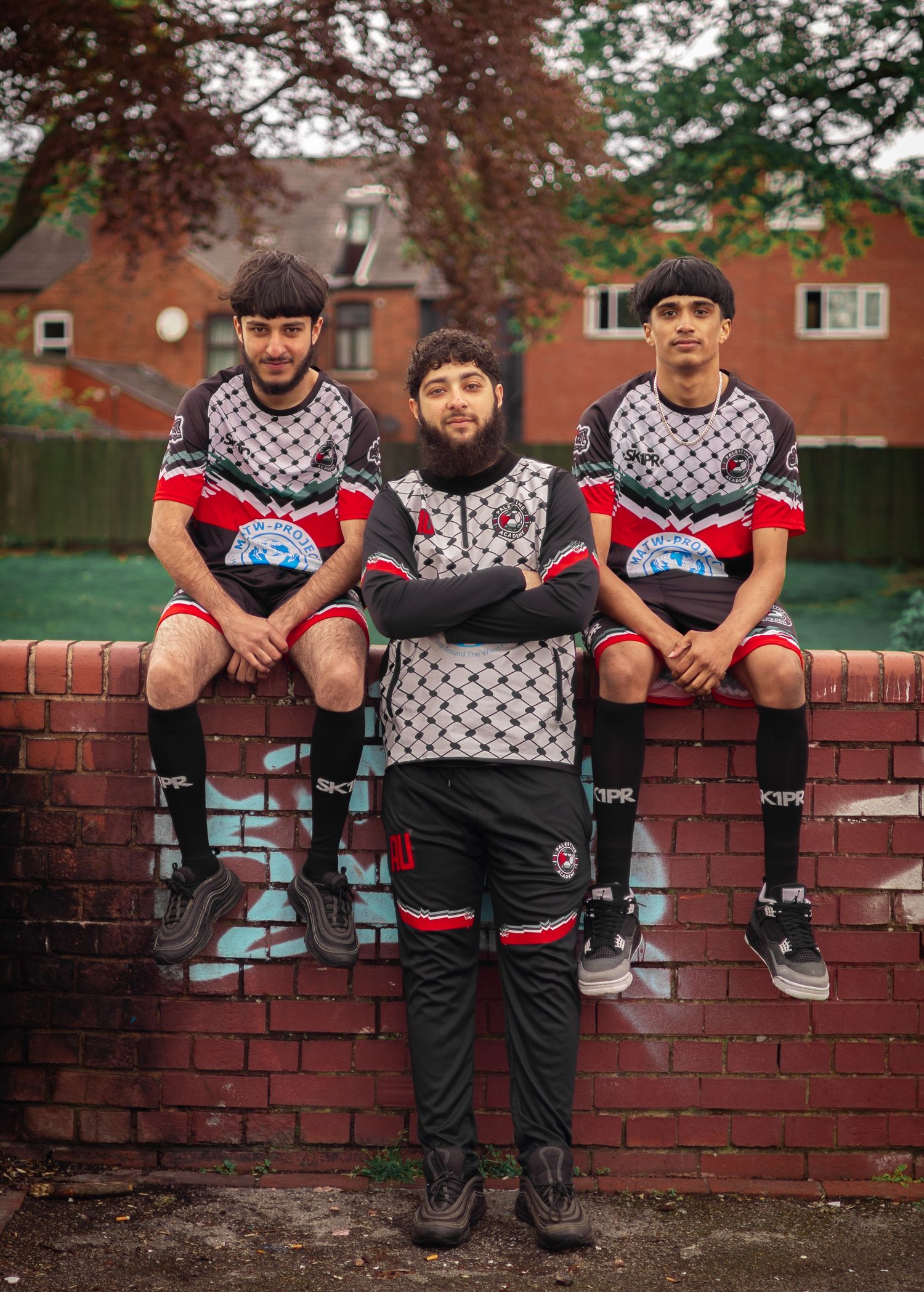 Three players in matching soccer uniforms posed on brick wall outdoors.