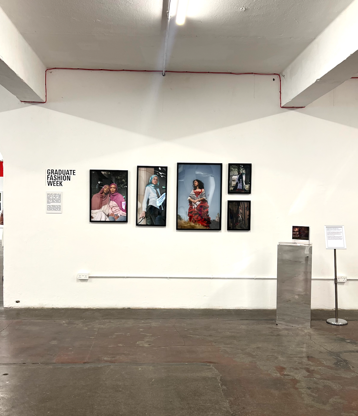Graduate Fashion Week exhibition display with framed fashion photography prints on white gallery wall in industrial space.