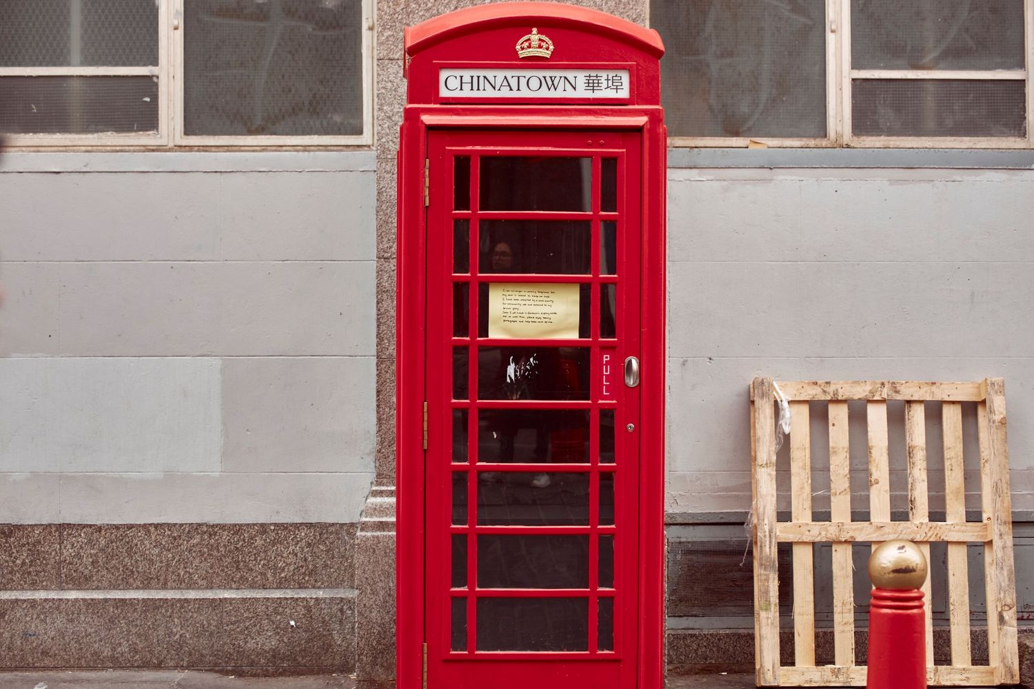 Classic red British phone booth against grey wall with wooden pallet.