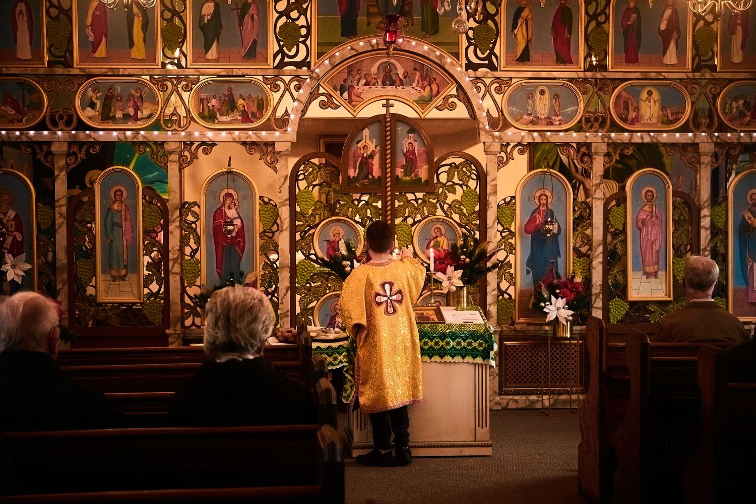 Traditional Orthodox church altar with gilded iconostasis and religious artwork illuminated in warm light.