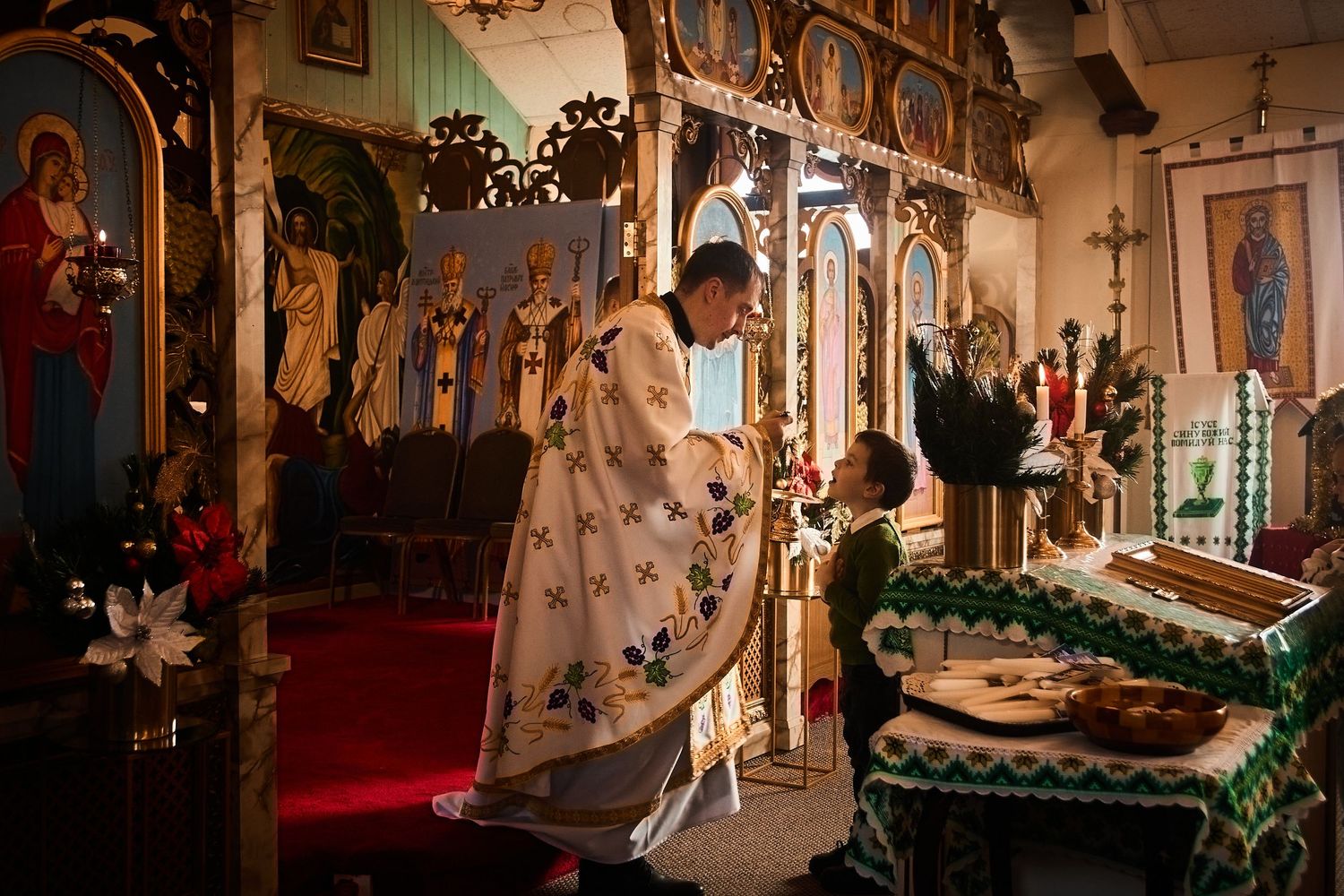 Interior of Orthodox church with elaborate iconostasis and seasonal greenery.