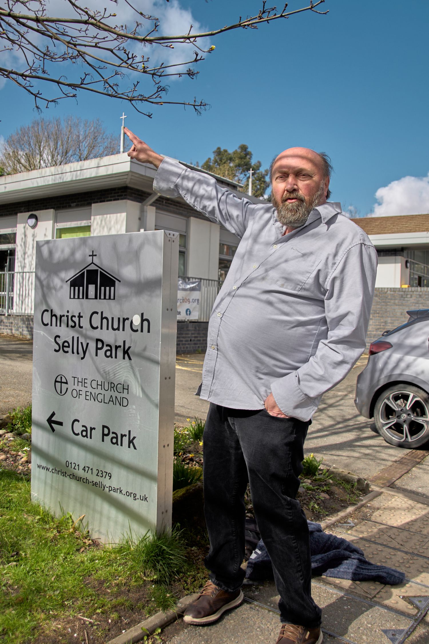 A person points while standing next to the Christ Church Selly Park directional sign.