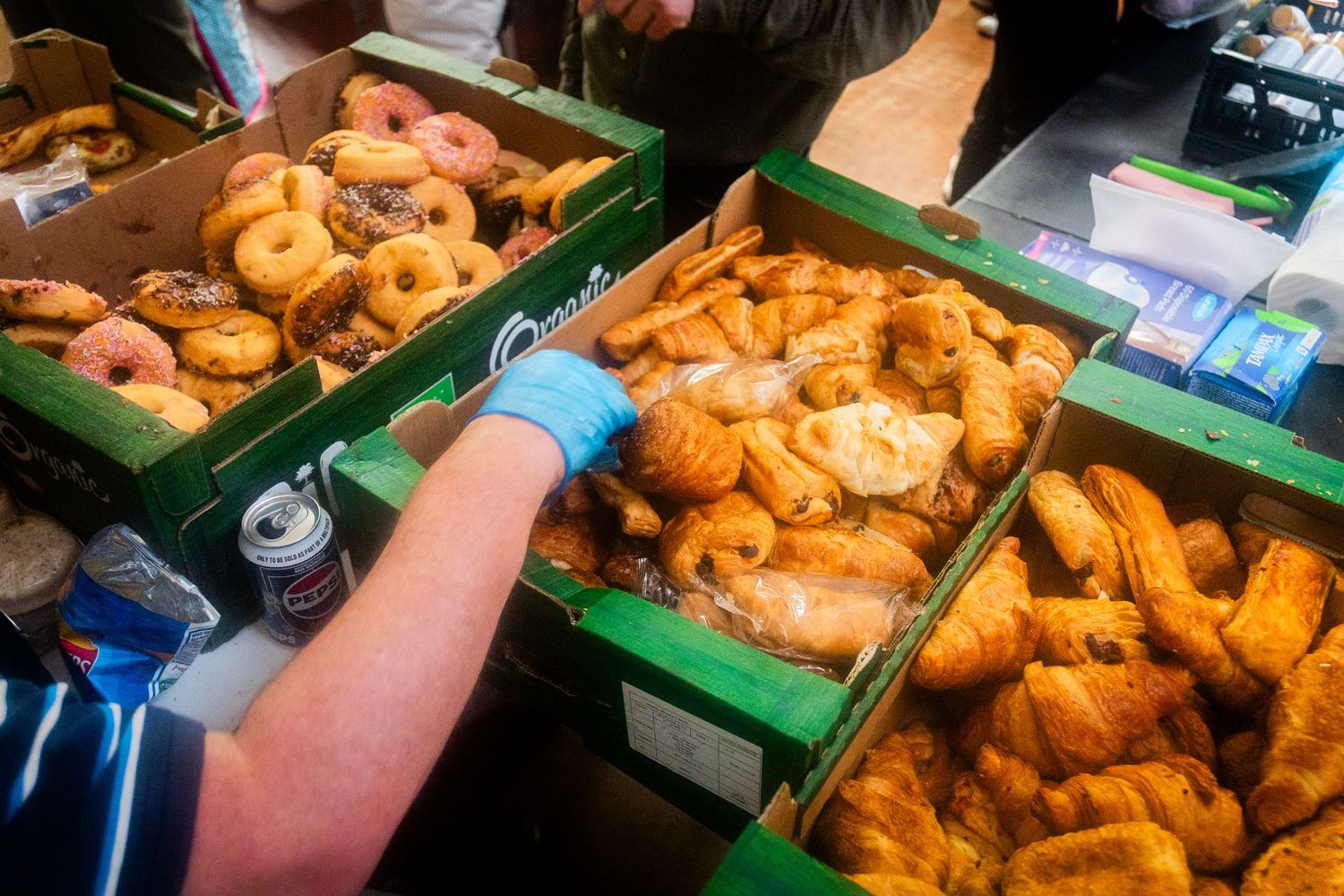 Volunteers wearing blue gloves sort fresh baked goods in green distribution crates.