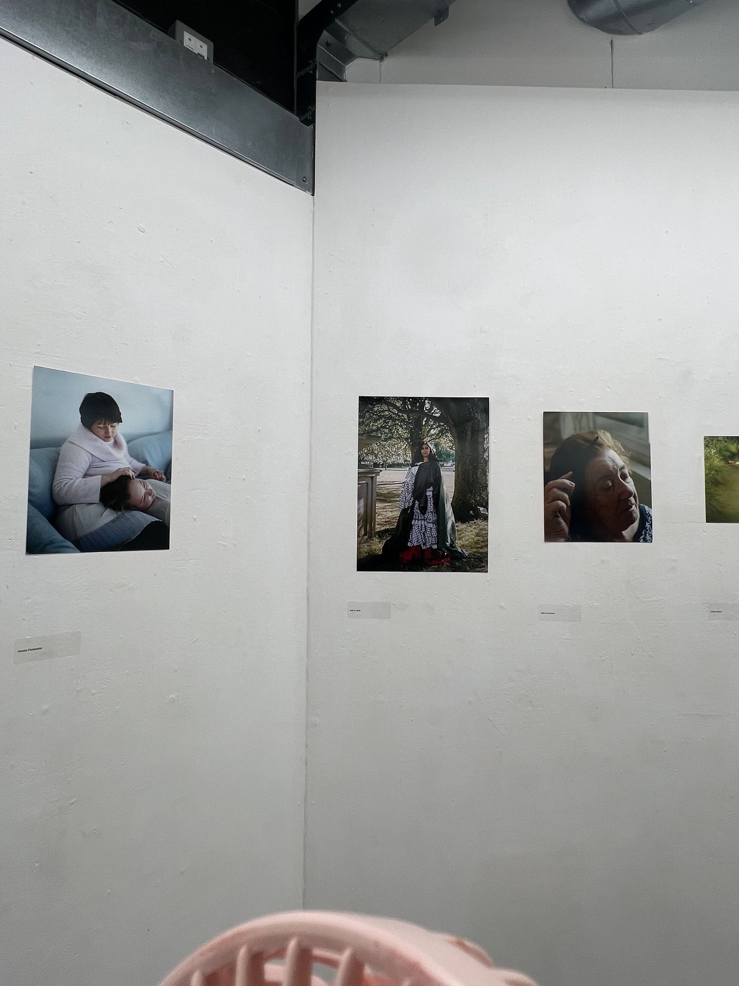 Art gallery wall displaying four photographs of people in various settings, mounted on white walls in an exhibition space.