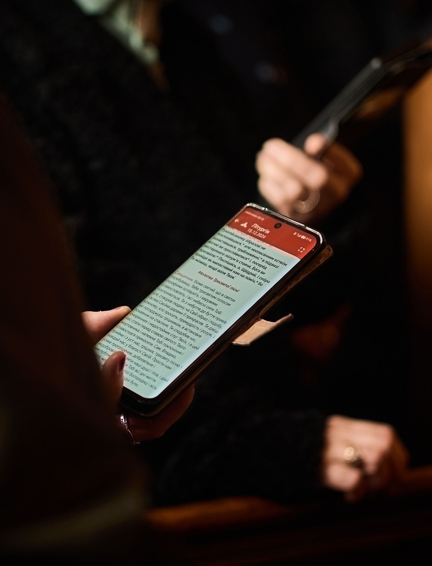 Person holding a smartphone displaying a red and white app interface with text content in a dimly lit setting.