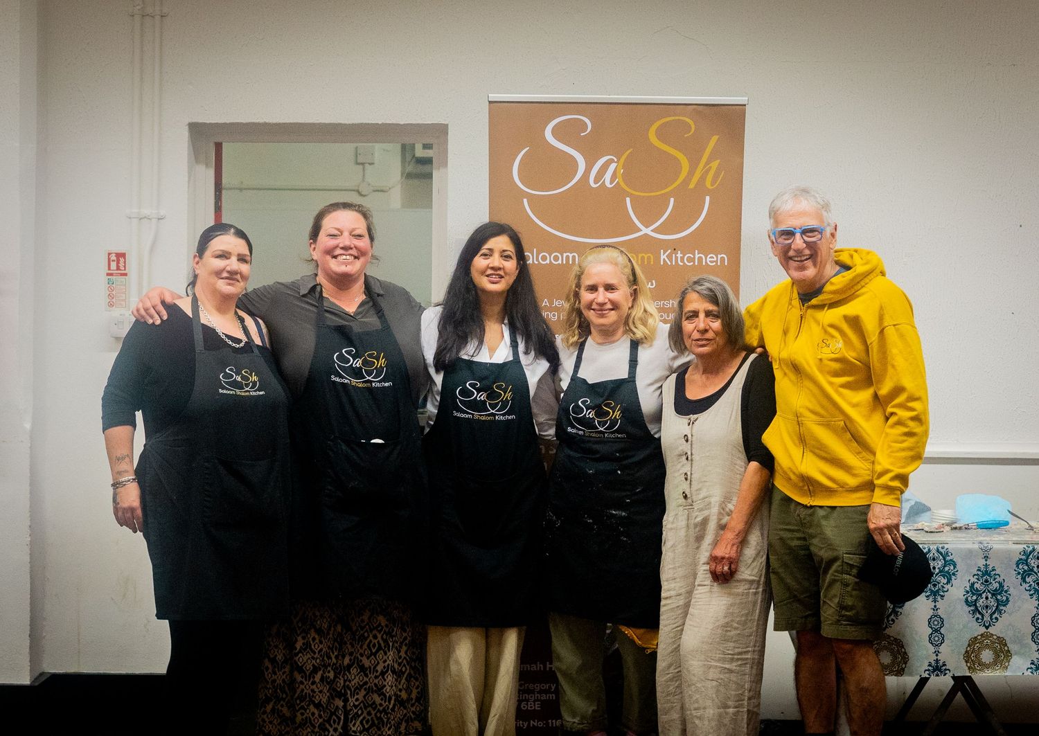 Restaurant team members posed together in front of SaSh Kitchen signage.