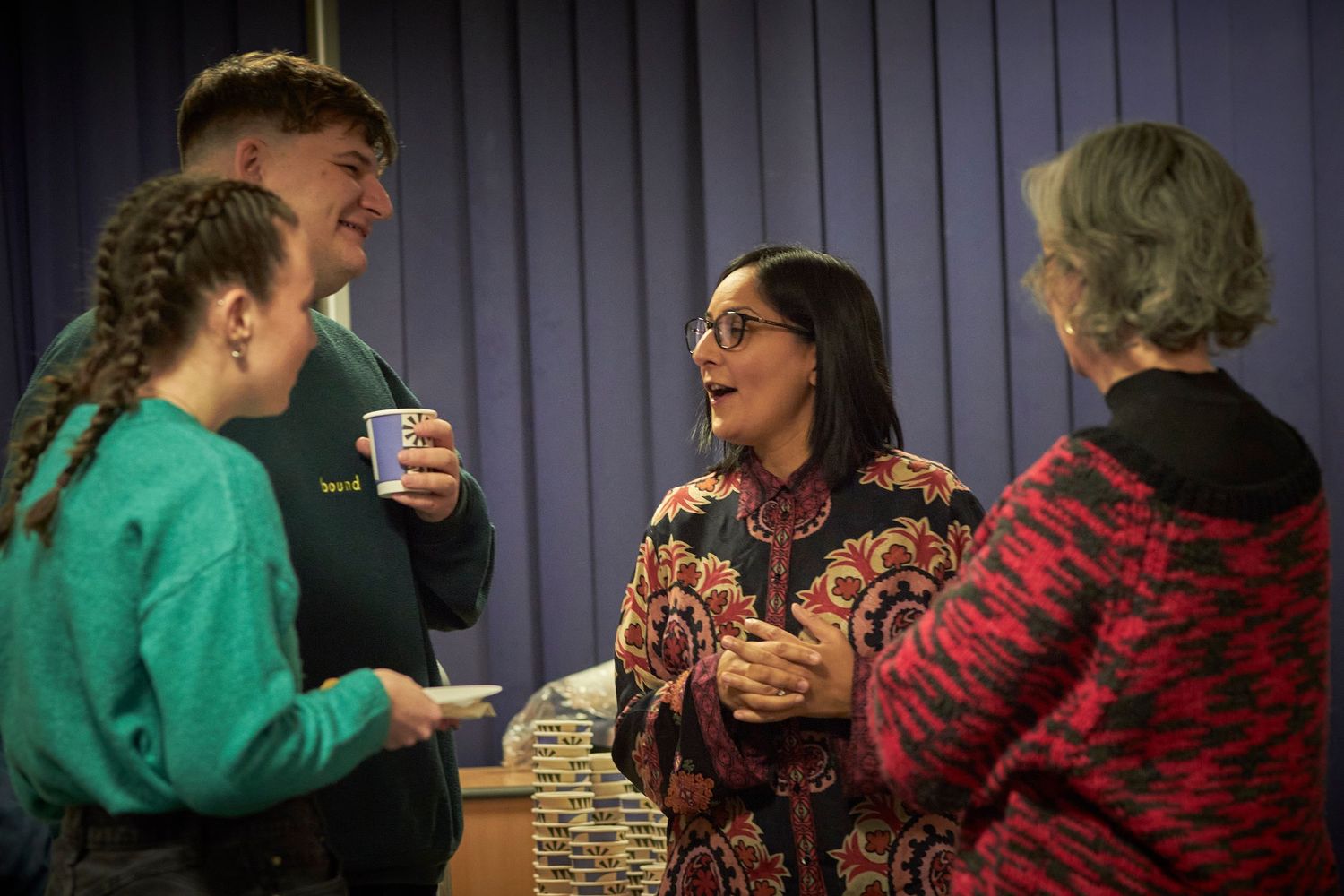 Group of people engaged in warm conversation while sharing coffee and tea at a casual indoor gathering.