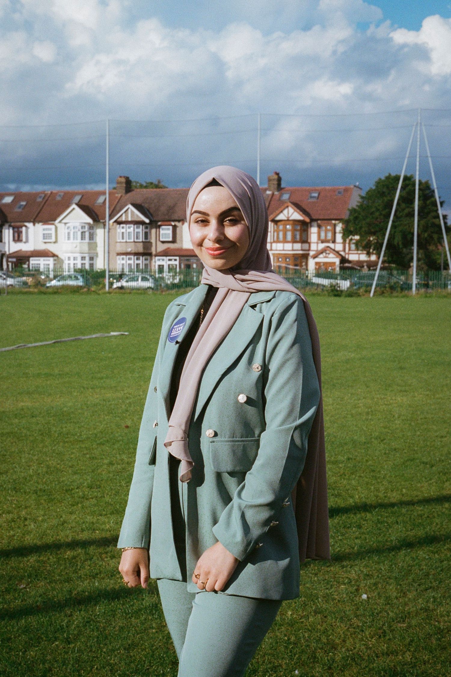 Fashion portrait in sage green suit against suburban landscape and blue sky.