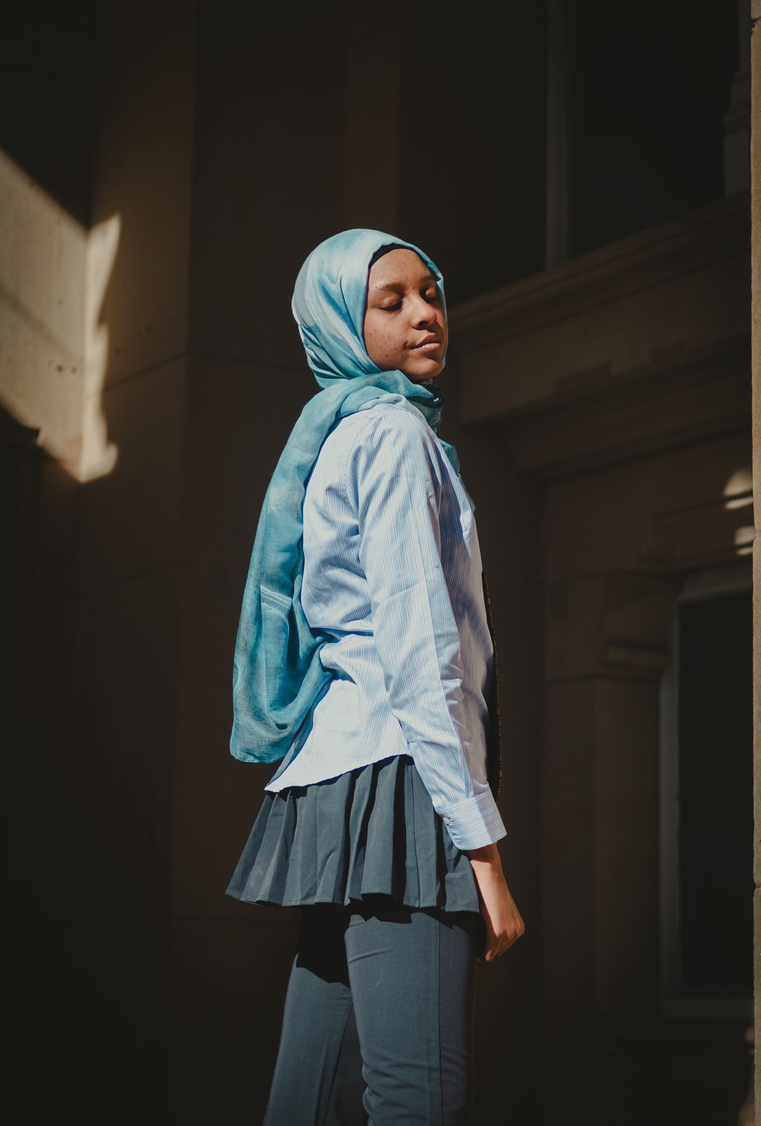 Side profile fashion shot highlighting a pleated skirt and light blue button-down shirt combination.