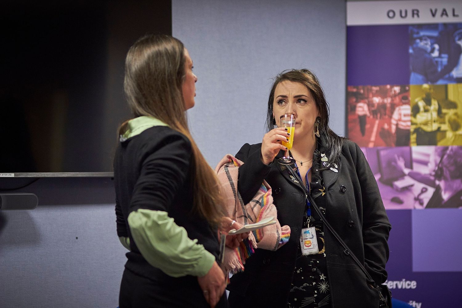 Professional colleagues stand in conversation during a business meeting in an office hallway.