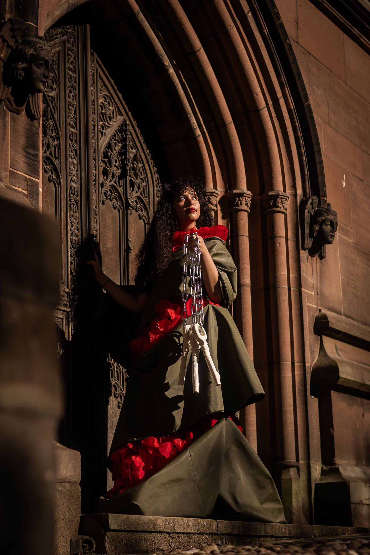 A couple in wedding attire poses romantically against gothic stone archways in dramatic lighting.
