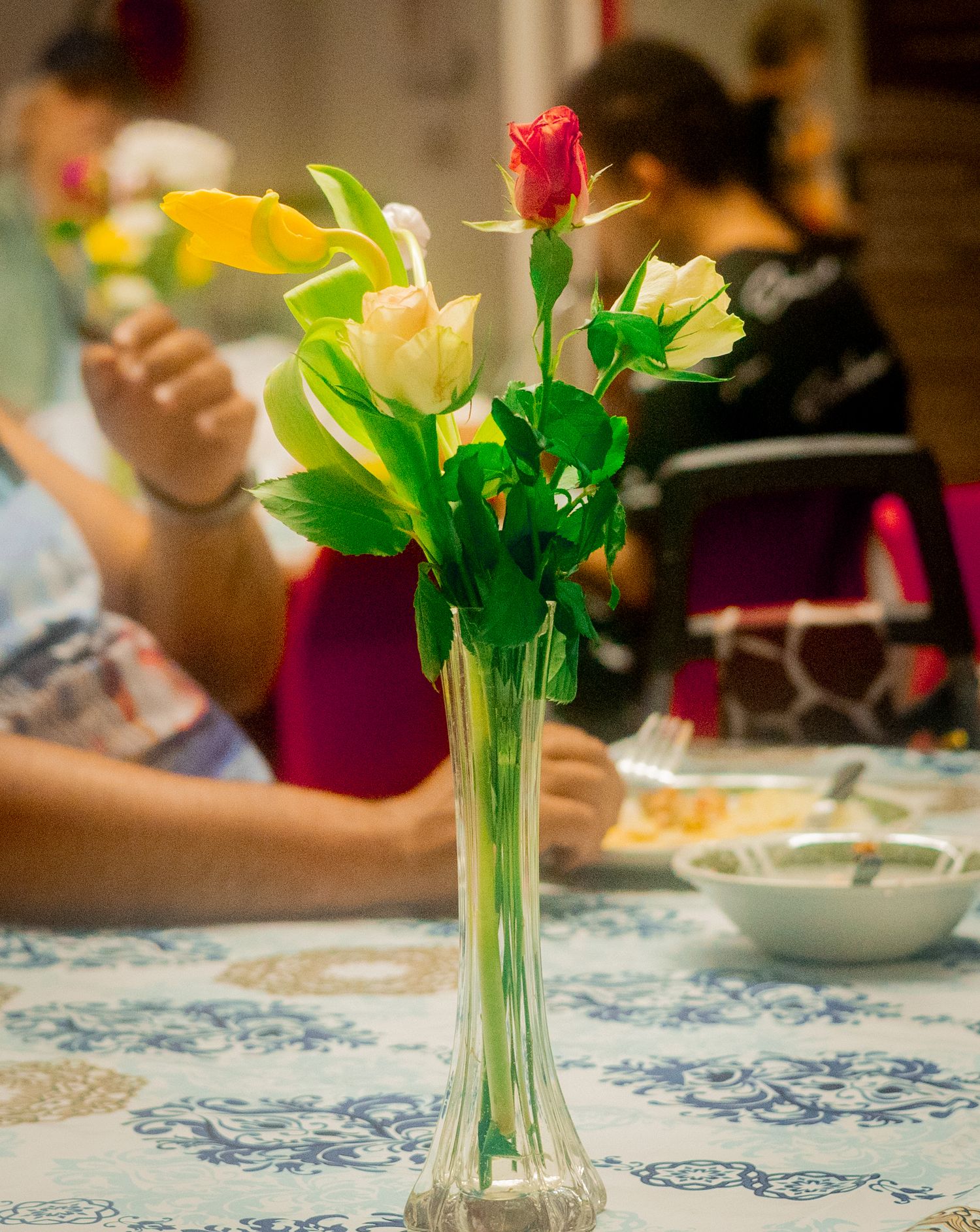 Colorful flowers in glass vases decorate a table with a blue and white patterned tablecloth.